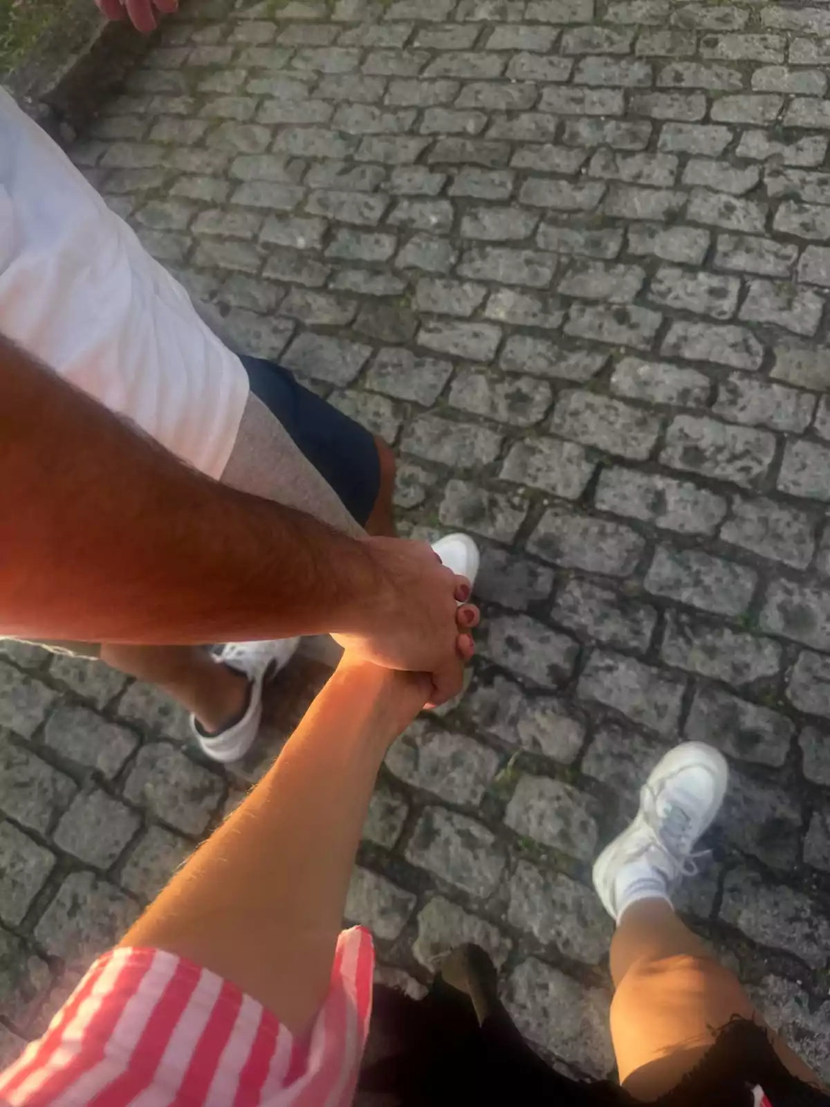 Dos personas tomadas de la mano caminando sobre un camino de adoquines Dos personas tomadas de la mano caminando sobre un camino de adoquines