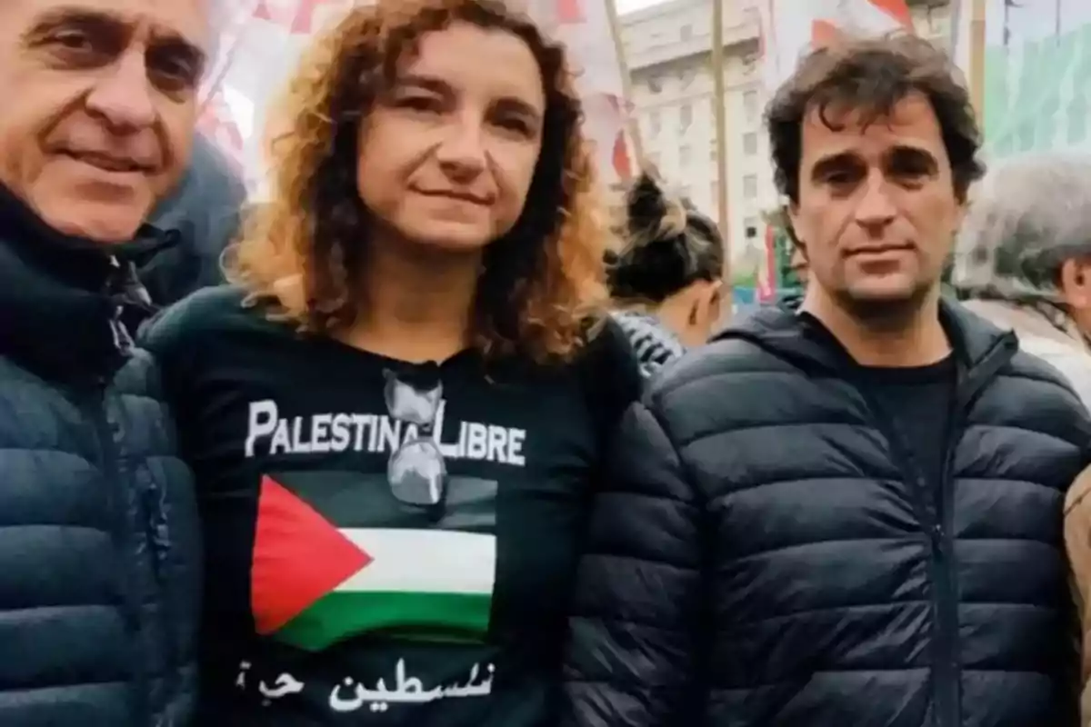 Tres personas posan juntas en una manifestación, una de ellas lleva una camiseta con el texto 