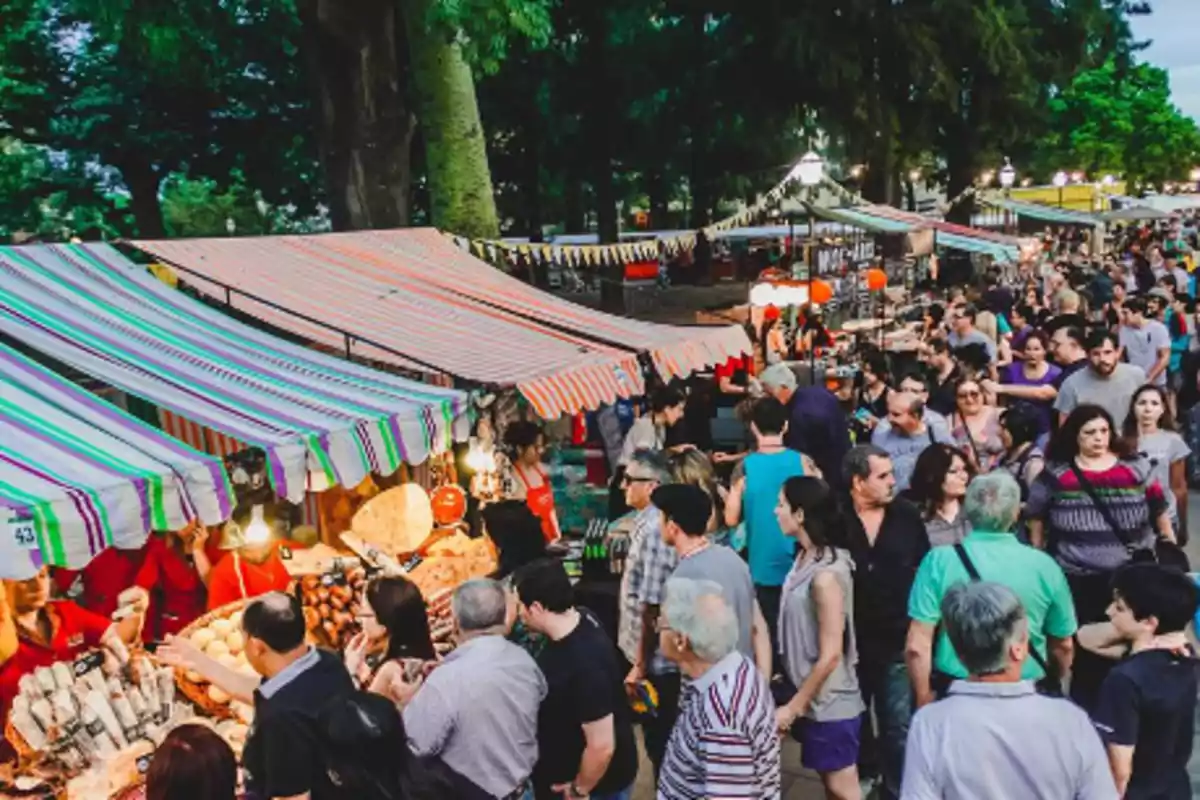 Una concurrida feria al aire libre con puestos de comida y muchas personas paseando.