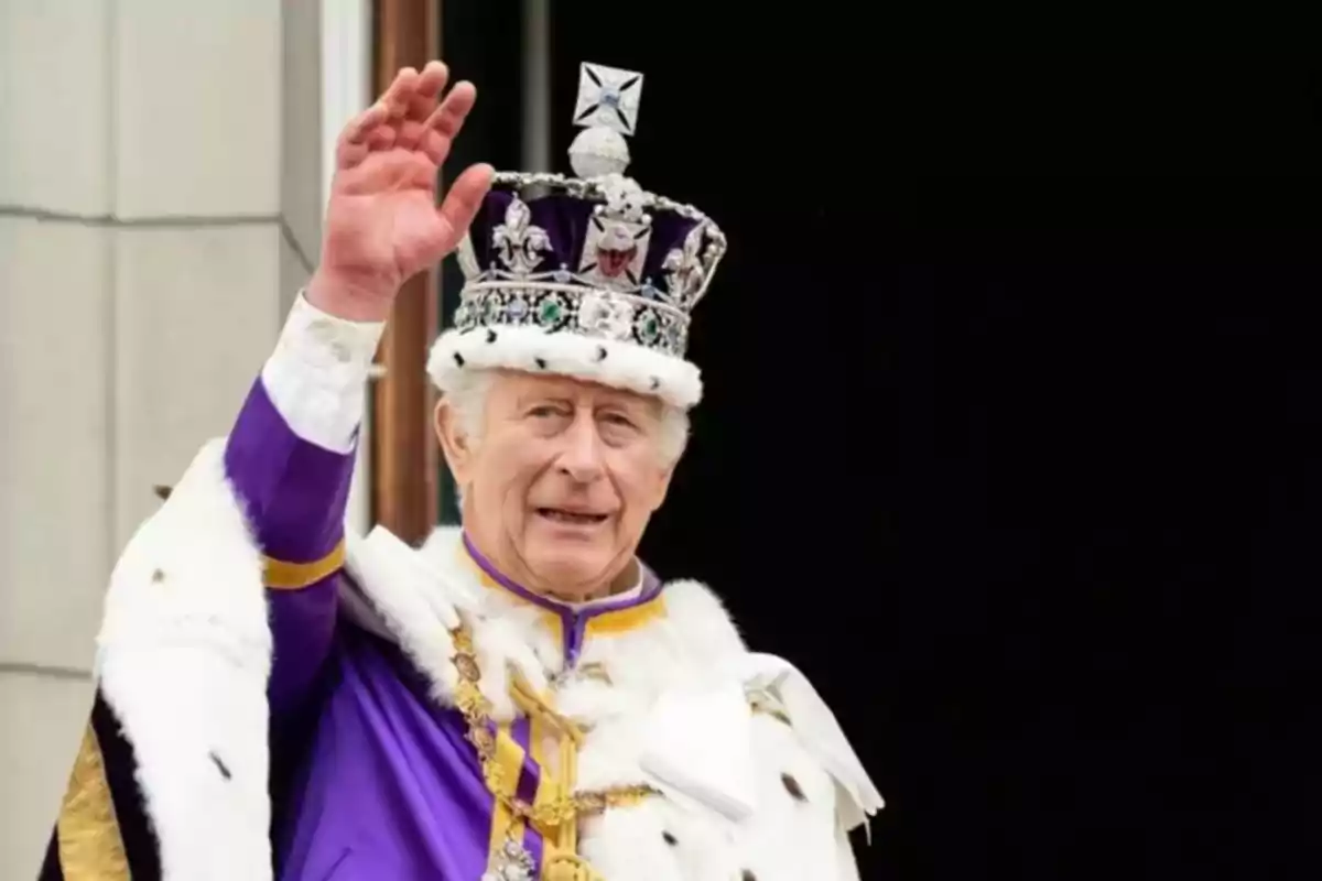 Un hombre con una corona y capa real levanta la mano en señal de saludo.