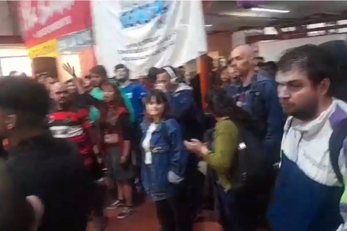 Un grupo de personas se encuentra reunido en un espacio interior, algunas de ellas sostienen pancartas y parecen estar participando en una manifestación o reunión.