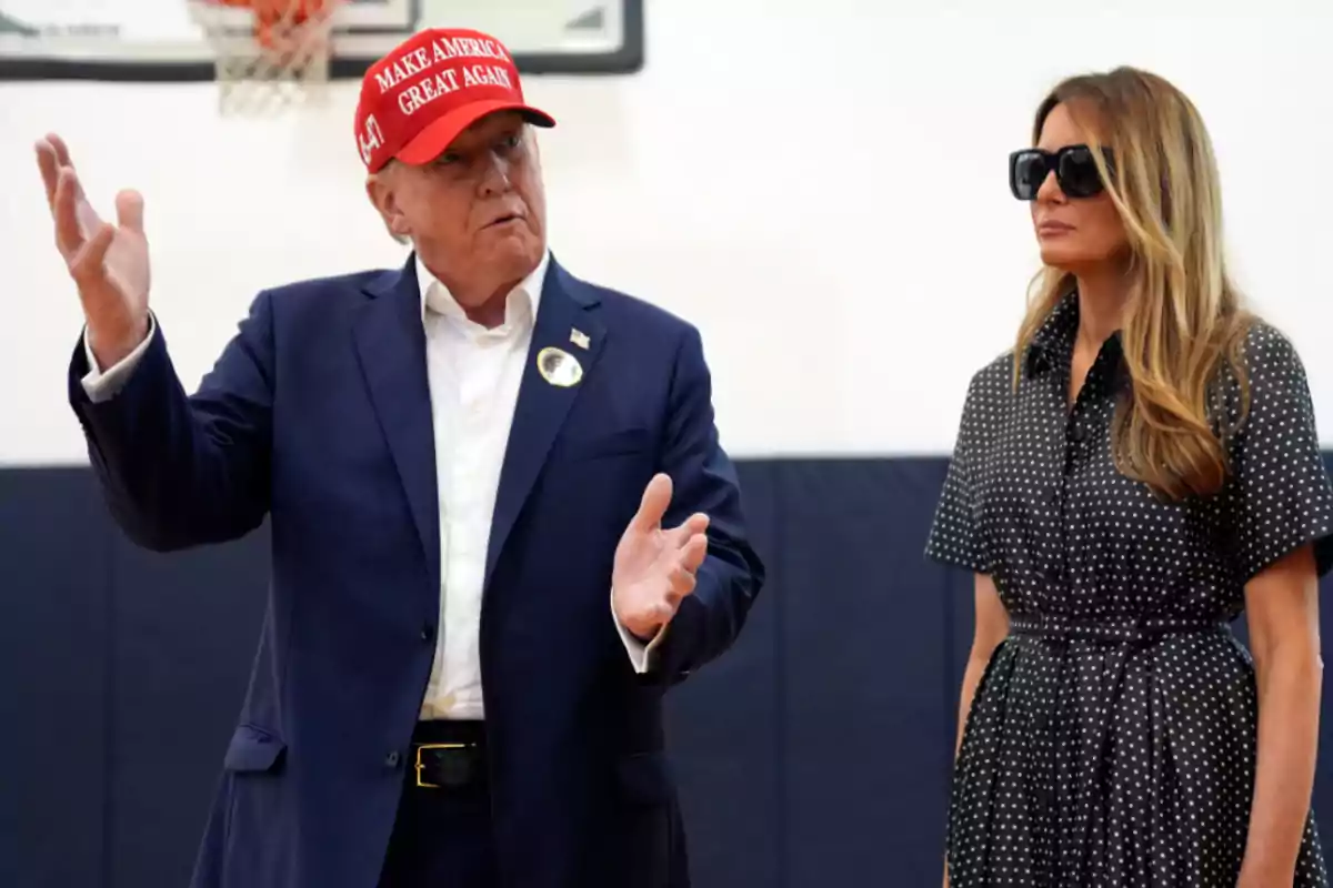 Un hombre con gorra roja y una mujer con gafas de sol están de pie en un gimnasio.