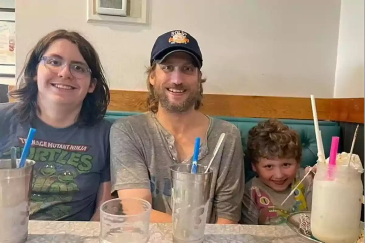 Tres personas sentadas en un restaurante disfrutando de batidos sonríen a la cámara.