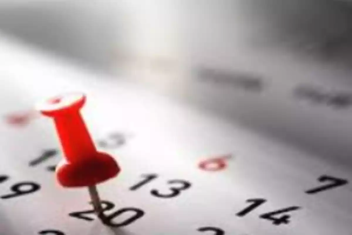 Un alfiler rojo clavado en un calendario sobre el número 20.