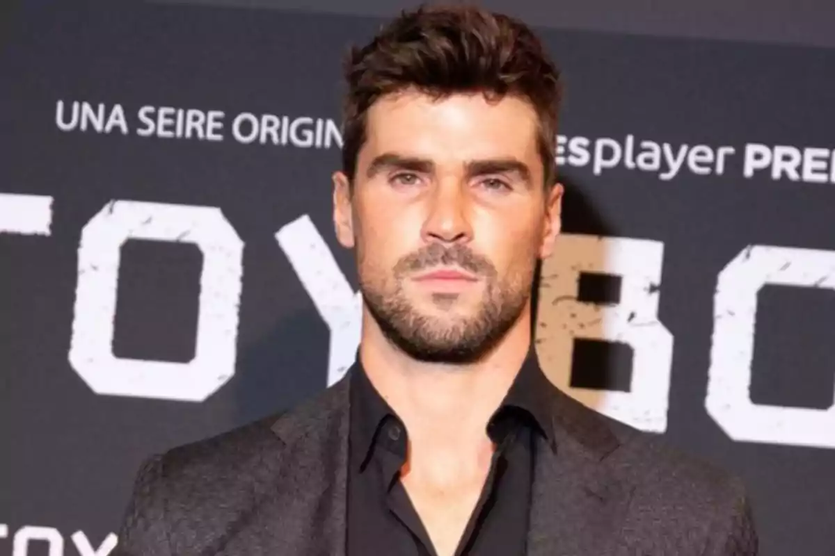 Hombre con barba y cabello oscuro en un evento con fondo de letras grandes.