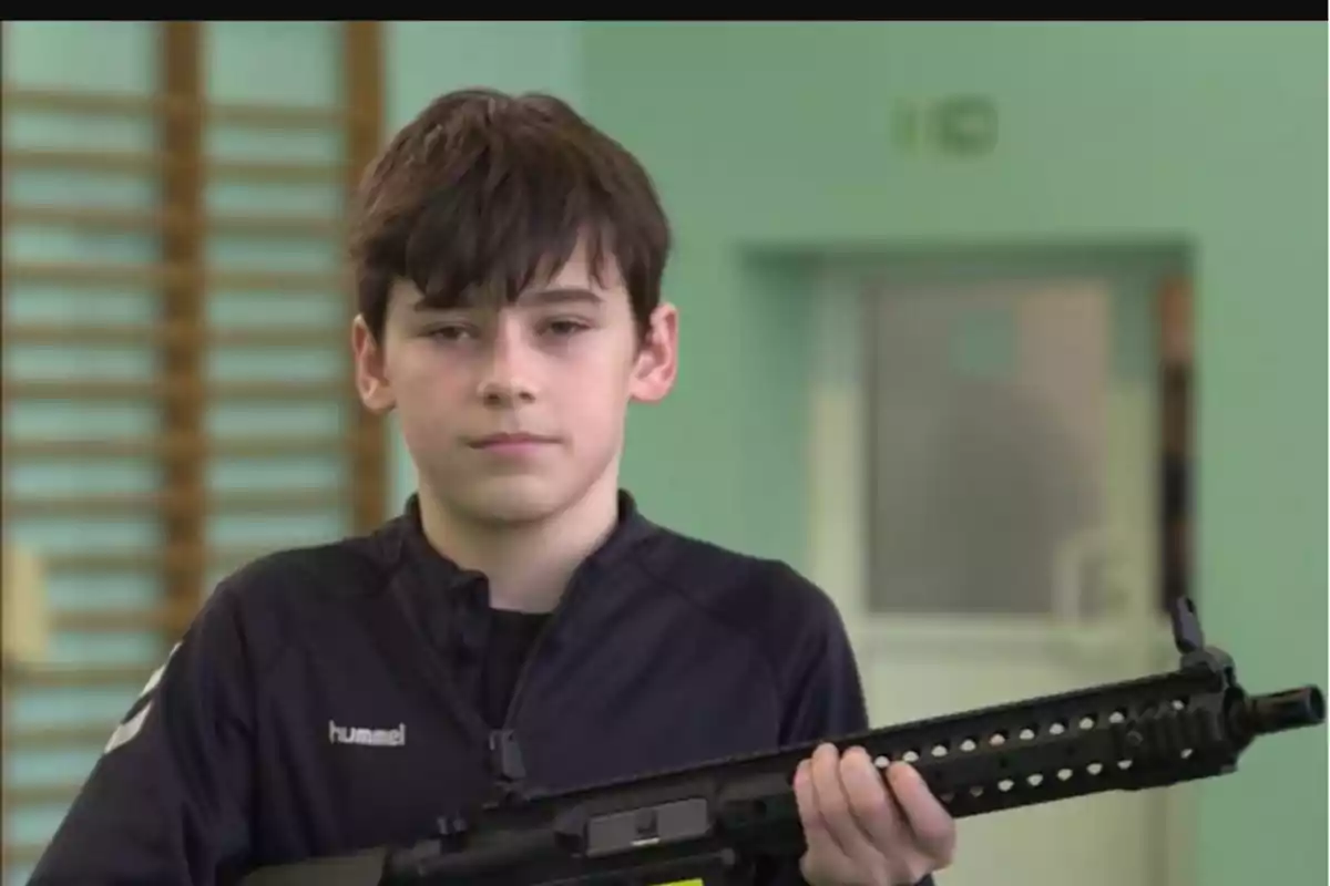 Un niño con cabello oscuro sostiene un objeto largo y negro en un entorno interior con paredes verdes.