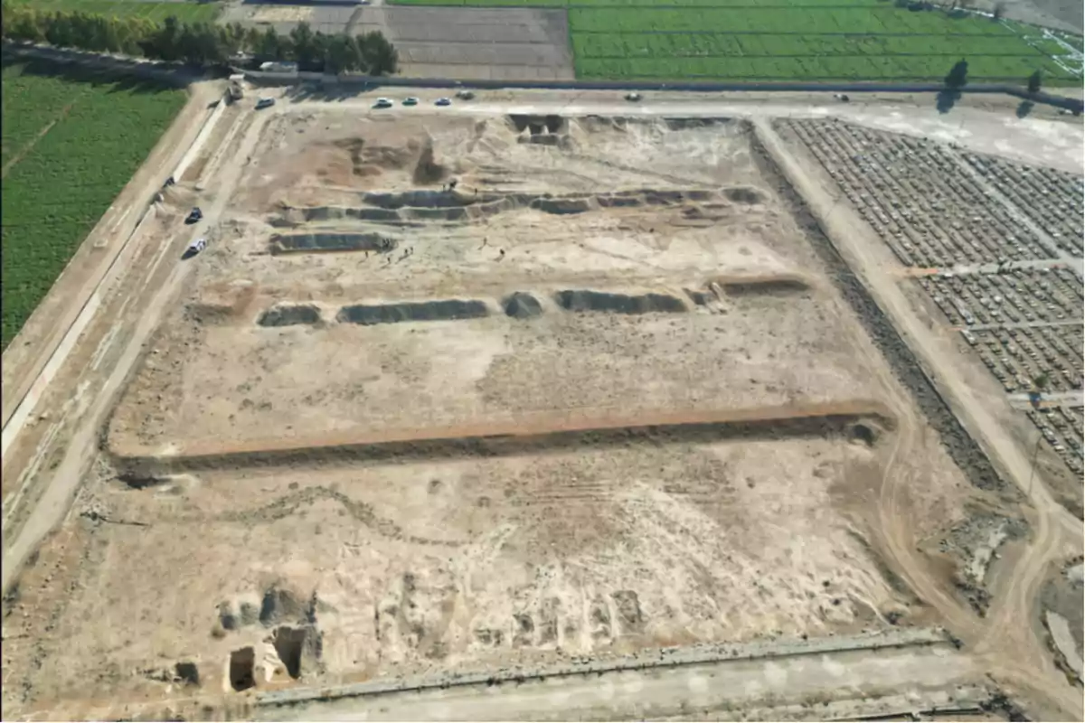 Vista aérea de un sitio arqueológico con excavaciones en un área desértica rodeada de campos verdes y caminos.