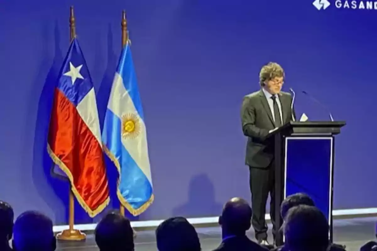 Un hombre de traje habla en un podio frente a un público, con las banderas de Chile y Argentina a su lado.