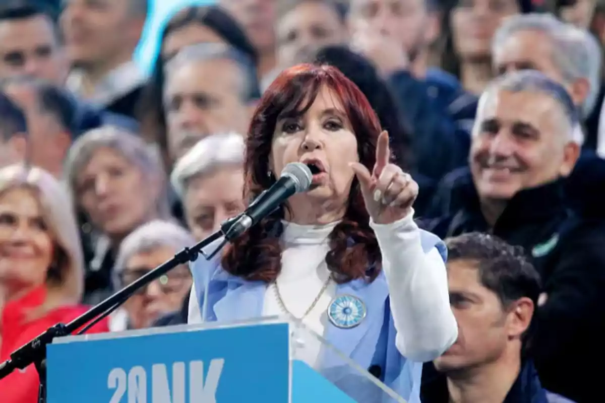 Una persona hablando en un mitin con un micrófono, rodeada de una multitud.