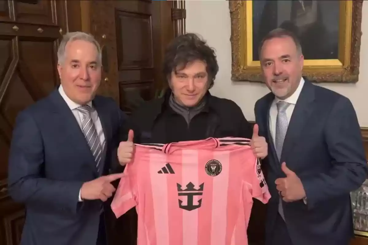 Tres personas posan juntas mientras sostienen una camiseta de fútbol rosa con un logotipo en el centro.