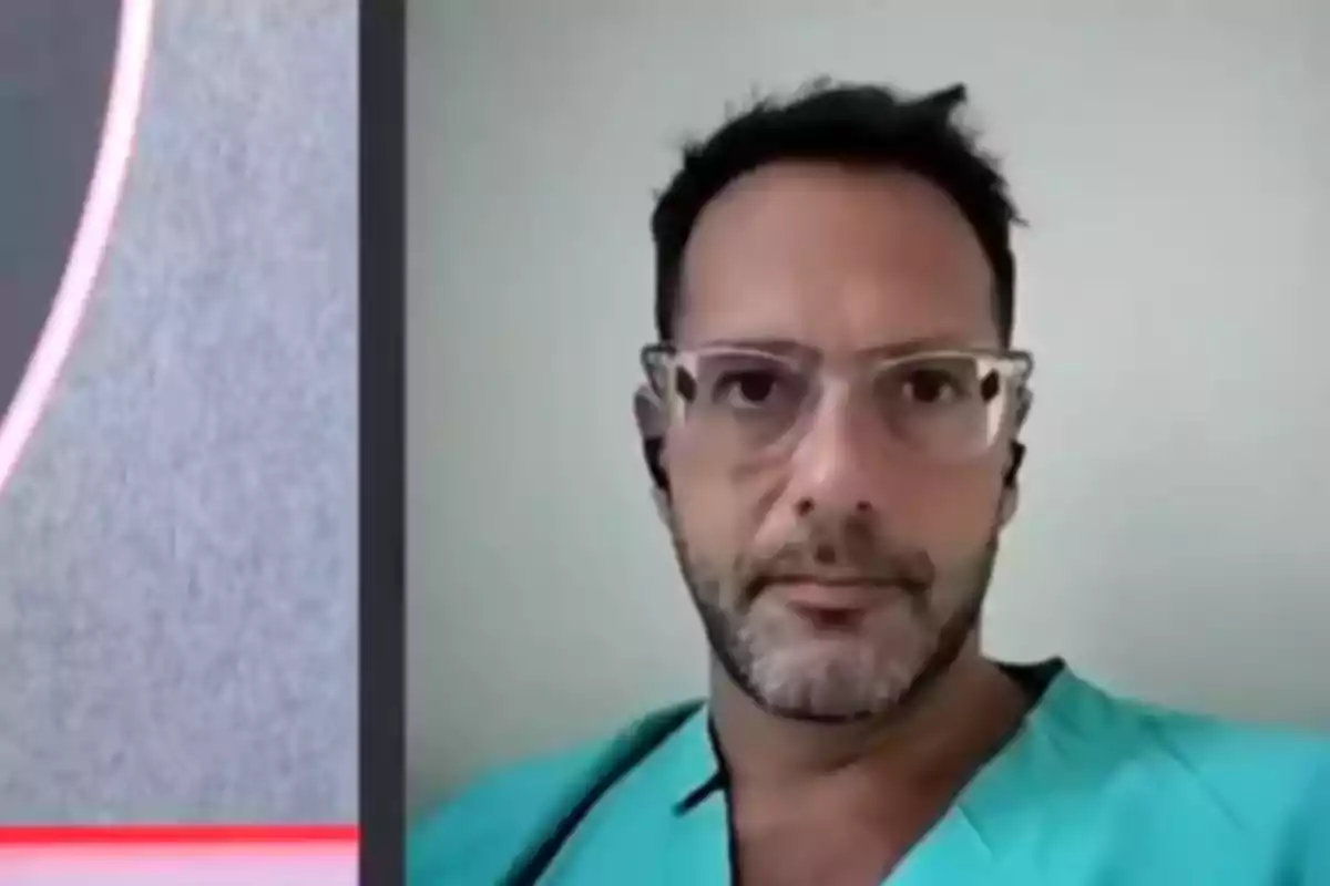 Un hombre con gafas y barba lleva puesto un uniforme médico de color verde.