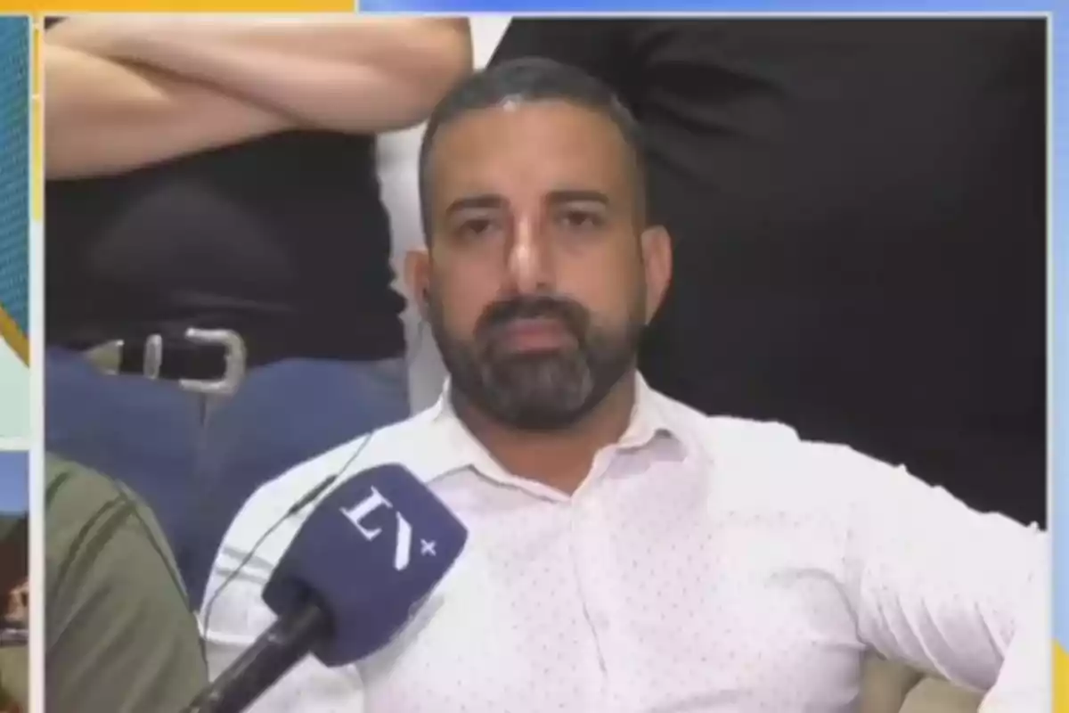 Un hombre con barba y camisa blanca está frente a un micrófono en una entrevista.