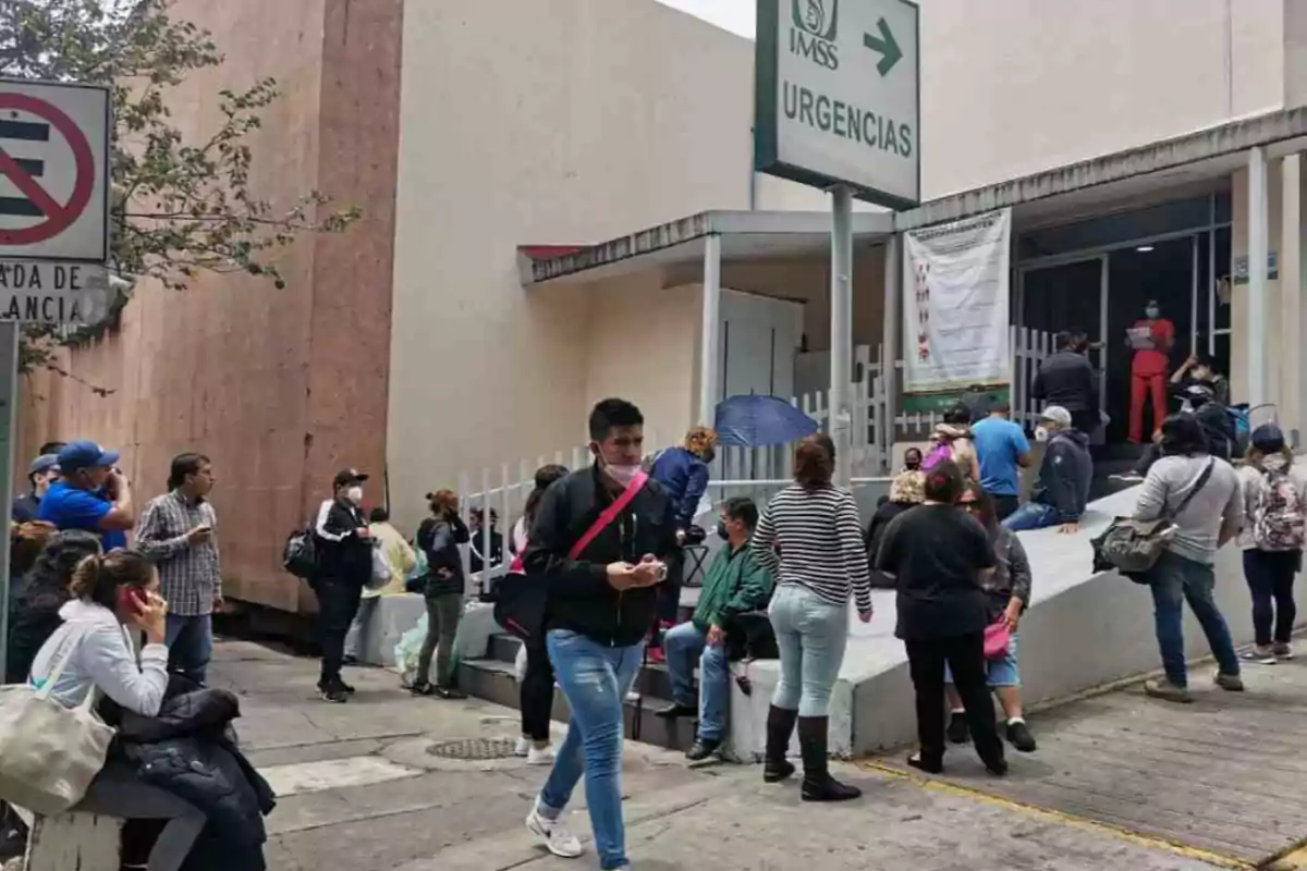 Personas esperando afuera de un hospital con un letrero de urgencias.