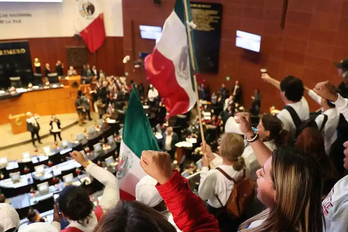 Un grupo de personas en un recinto legislativo levantan banderas de México y puños en señal de protesta o celebración.