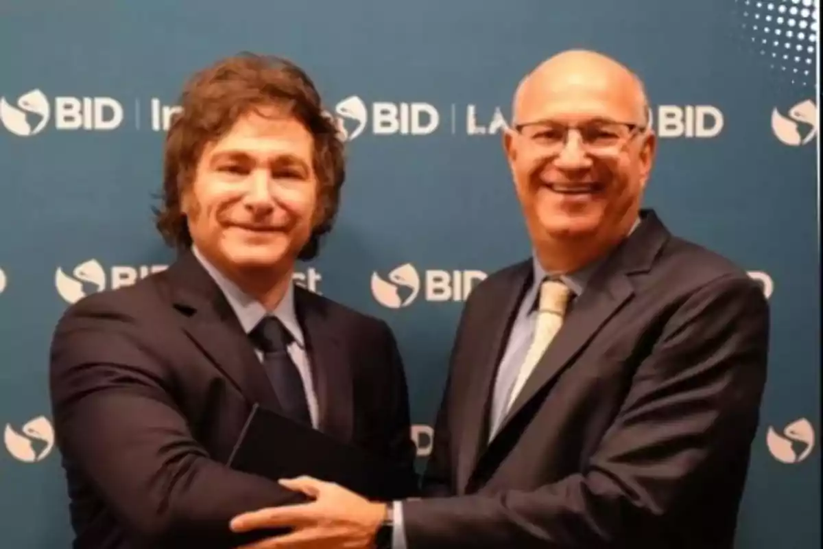 Dos personas de traje se dan la mano frente a un fondo con logotipos del BID.