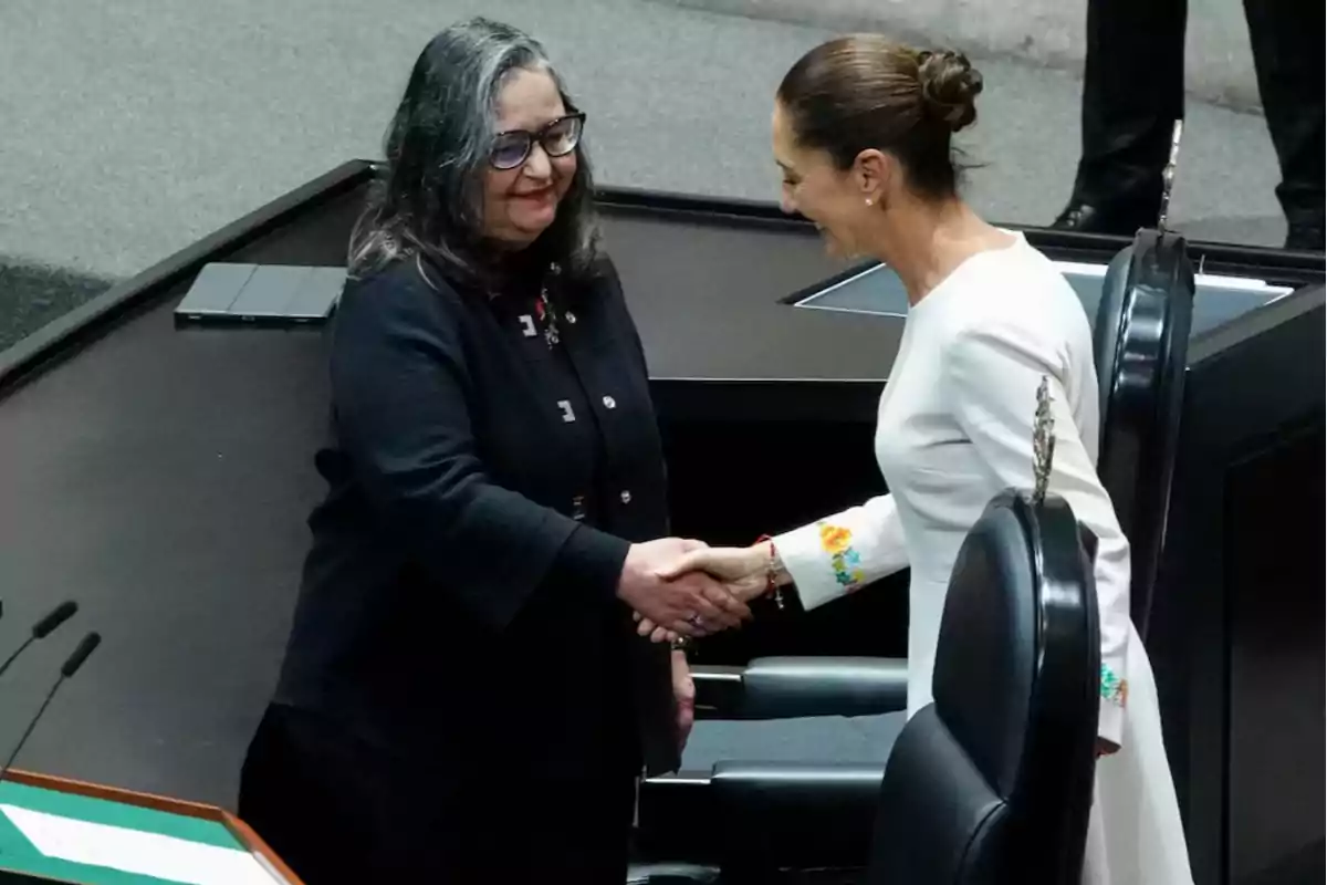 Dos mujeres dándose la mano en un entorno formal.