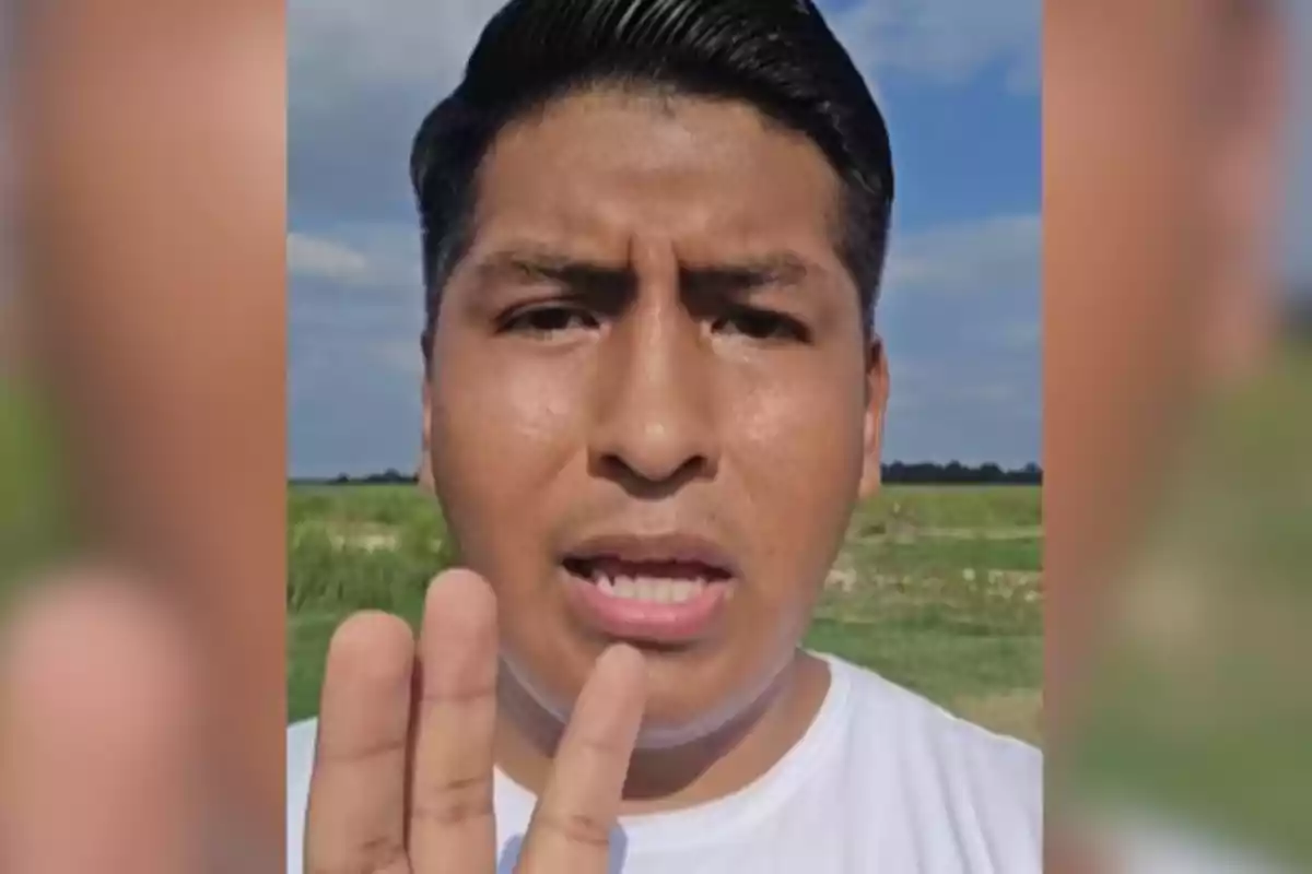 Un hombre joven con cabello oscuro está al aire libre levantando tres dedos de su mano frente a la cámara.