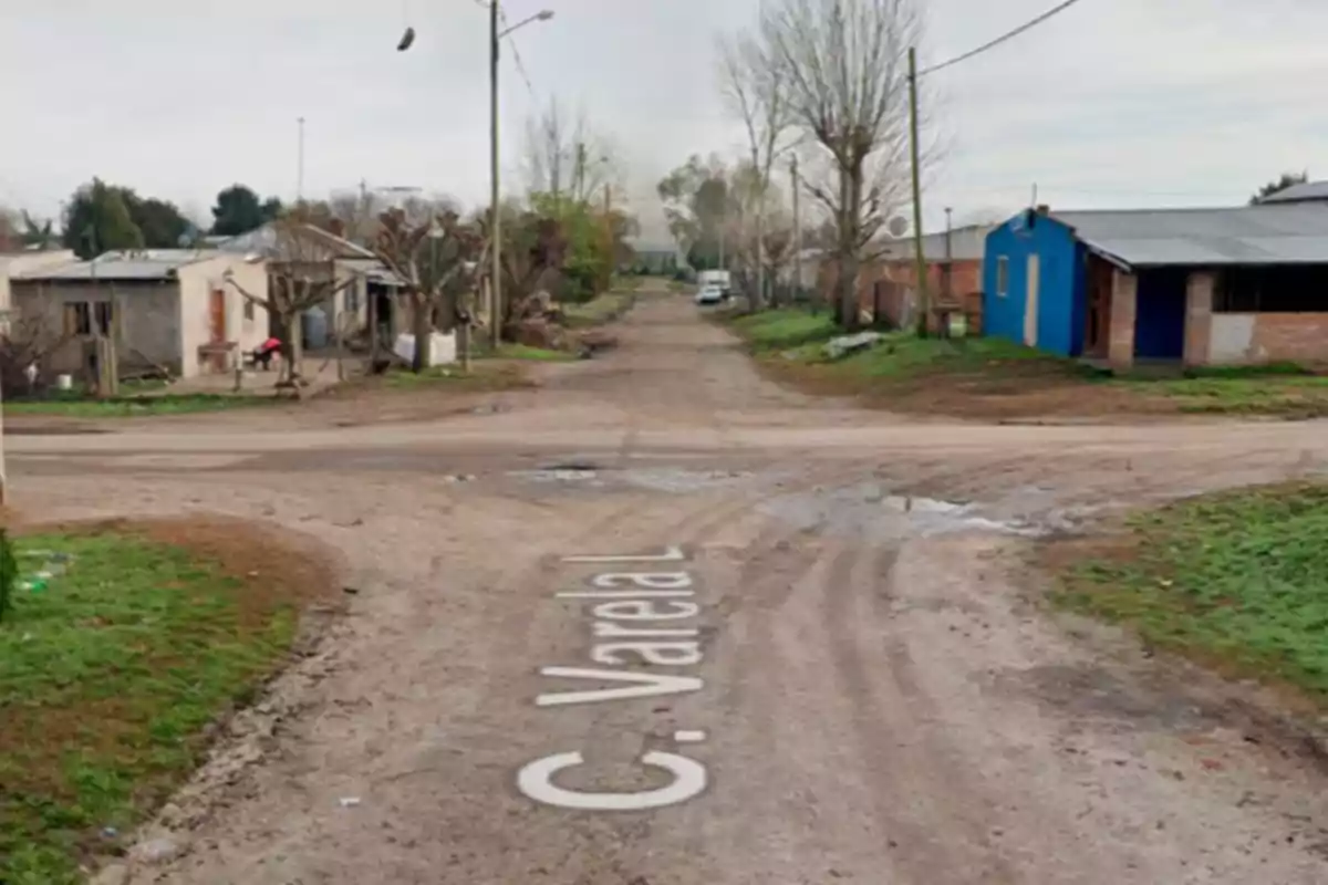 Una intersección de caminos de tierra en una zona rural con casas a los lados y árboles sin hojas.