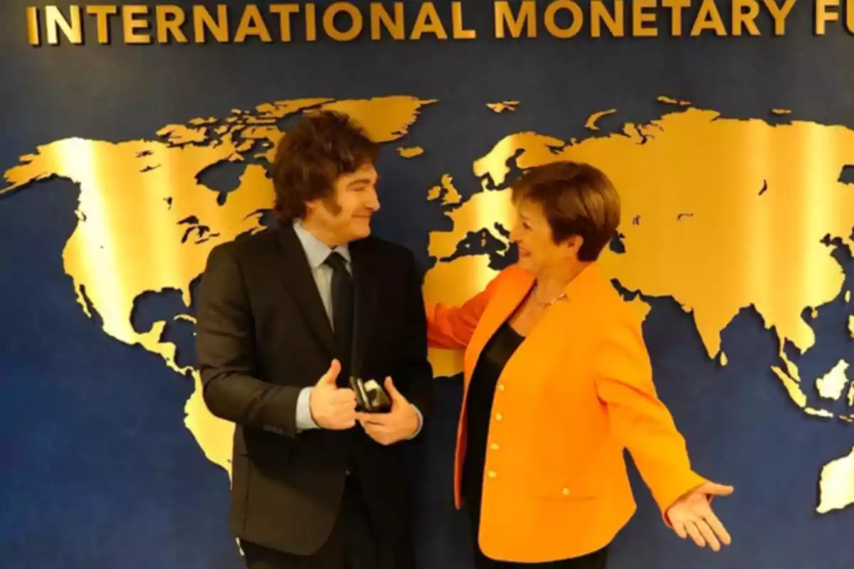 Two people talking in front of a golden map on a blue wall with the text "International Monetary Fund" above.