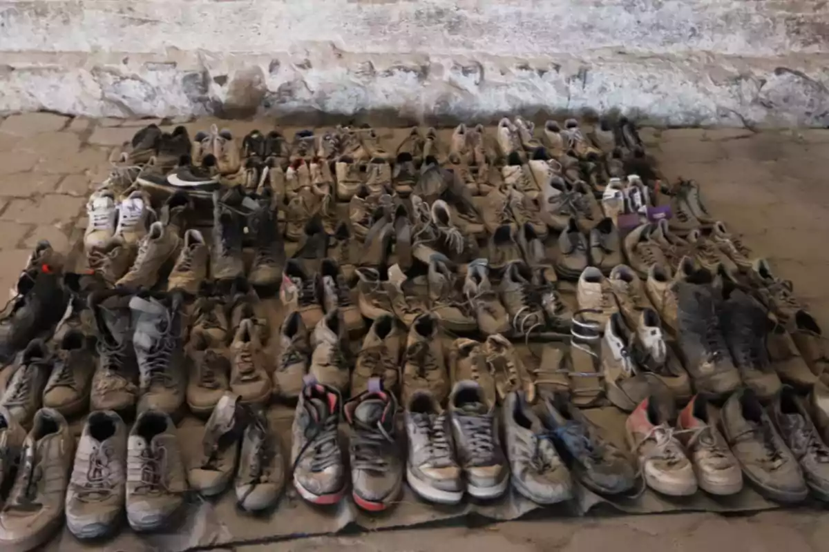 Una colección de zapatos deportivos desgastados y sucios organizados en filas sobre un suelo de piedra. Una colección de zapatos deportivos desgastados y sucios organizados en filas sobre un suelo de piedra.