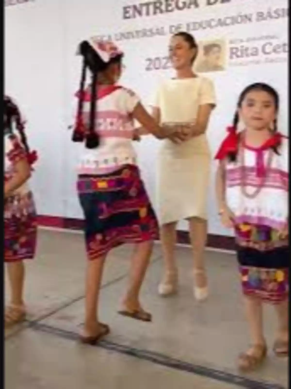 Un grupo de niñas con trajes tradicionales participa en un evento escolar, donde una mujer les entrega un reconocimiento. Un grupo de niñas con trajes tradicionales participa en un evento escolar, donde una mujer les entrega un reconocimiento.