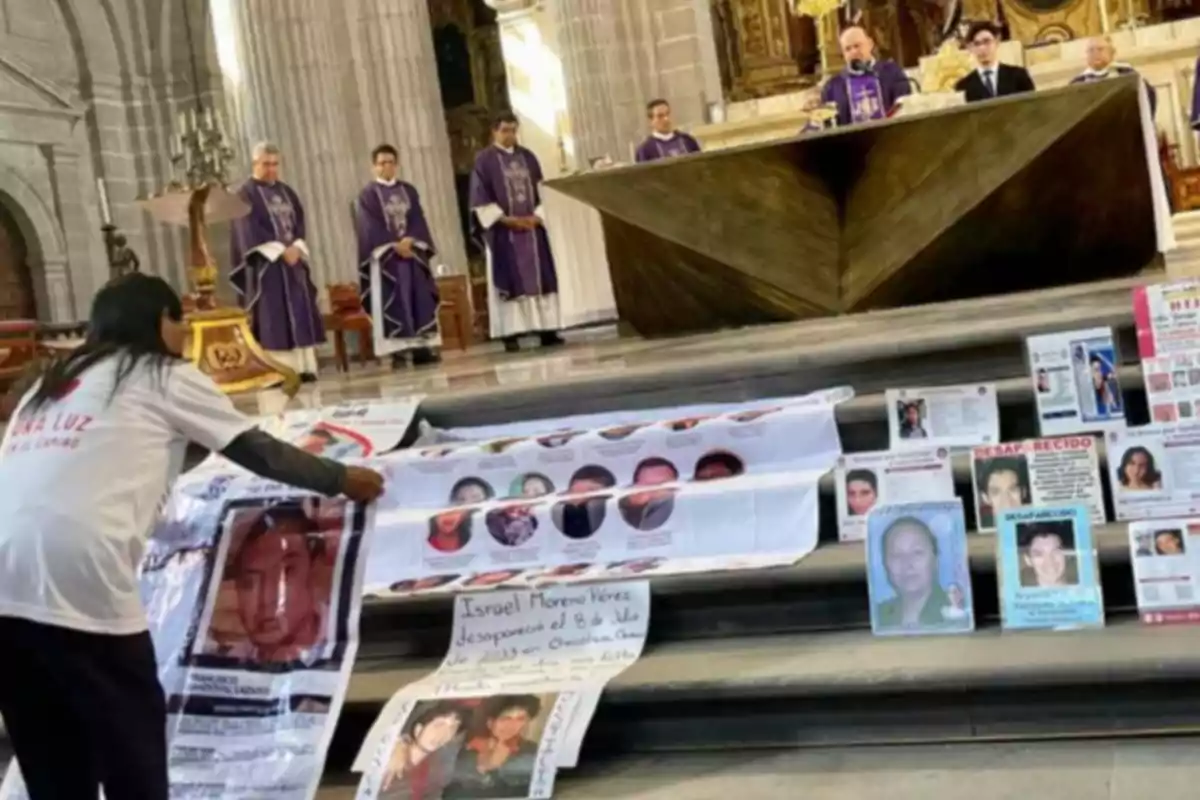 A person places posters with photos of missing people on the steps of an altar in a church, while several priests dressed in purple robes watch from the background.