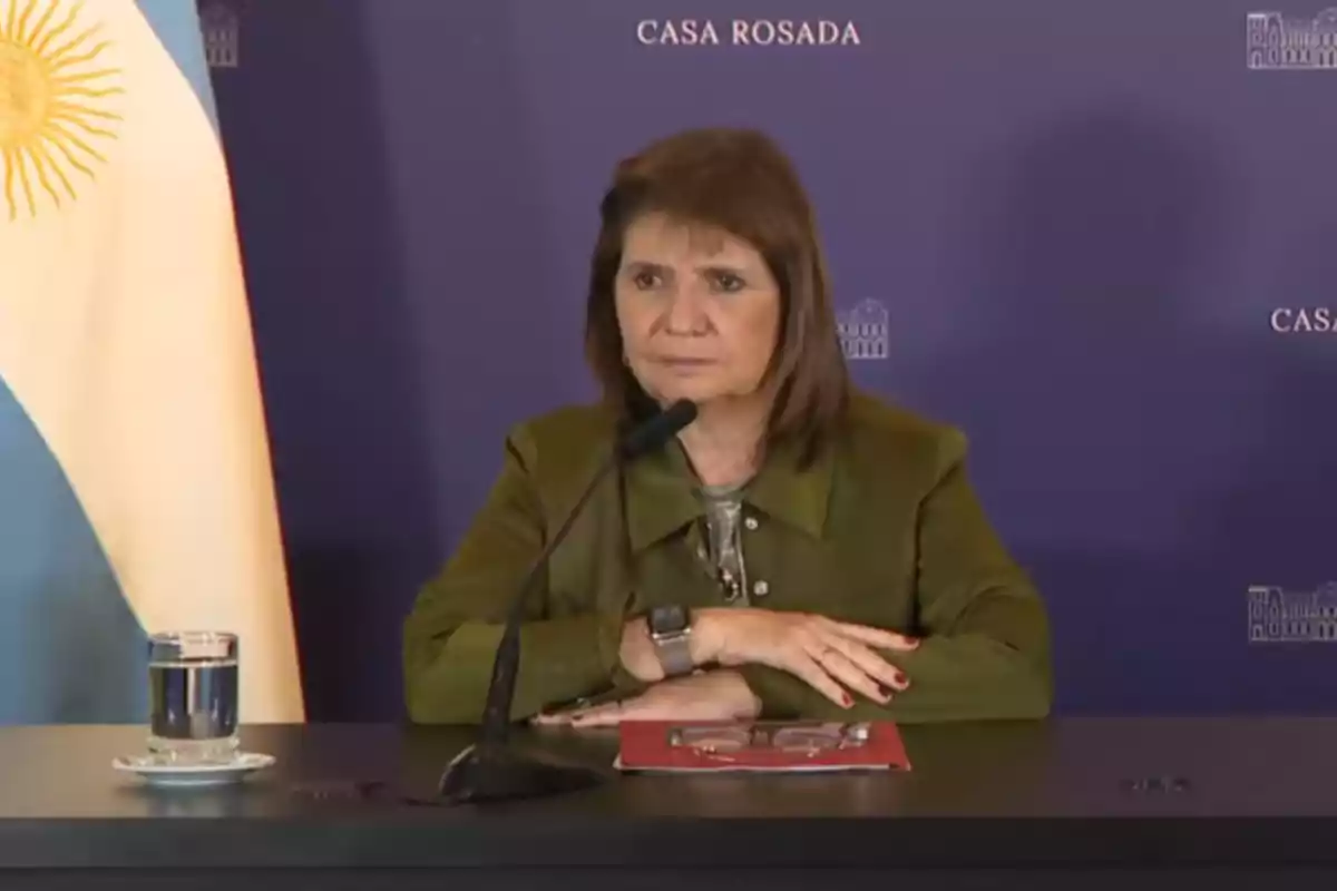 Una persona en una conferencia de prensa en la Casa Rosada con una bandera de Argentina al lado.