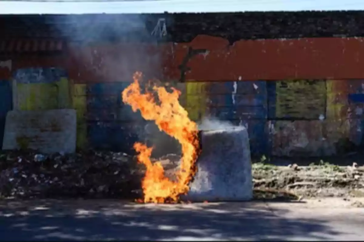 A block of concrete on fire in front of a worn and colorful wall.