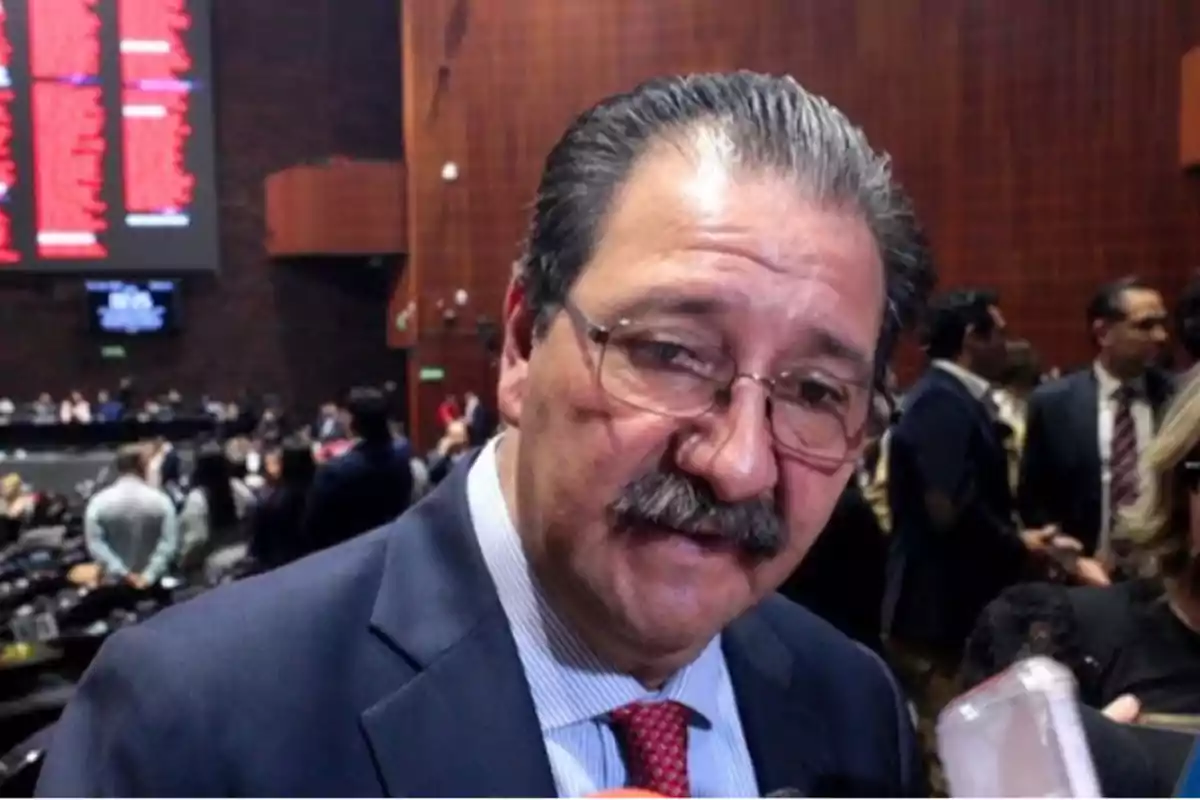 Un hombre con bigote y gafas en un entorno de conferencia o reunión formal. Un hombre con bigote y gafas en un entorno de conferencia o reunión formal.