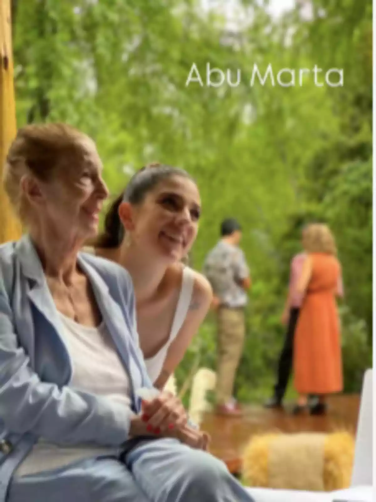 Dos personas sonríen mientras están sentadas al aire libre con un fondo verde y borroso. Dos personas sonríen mientras están sentadas al aire libre con un fondo verde y borroso.