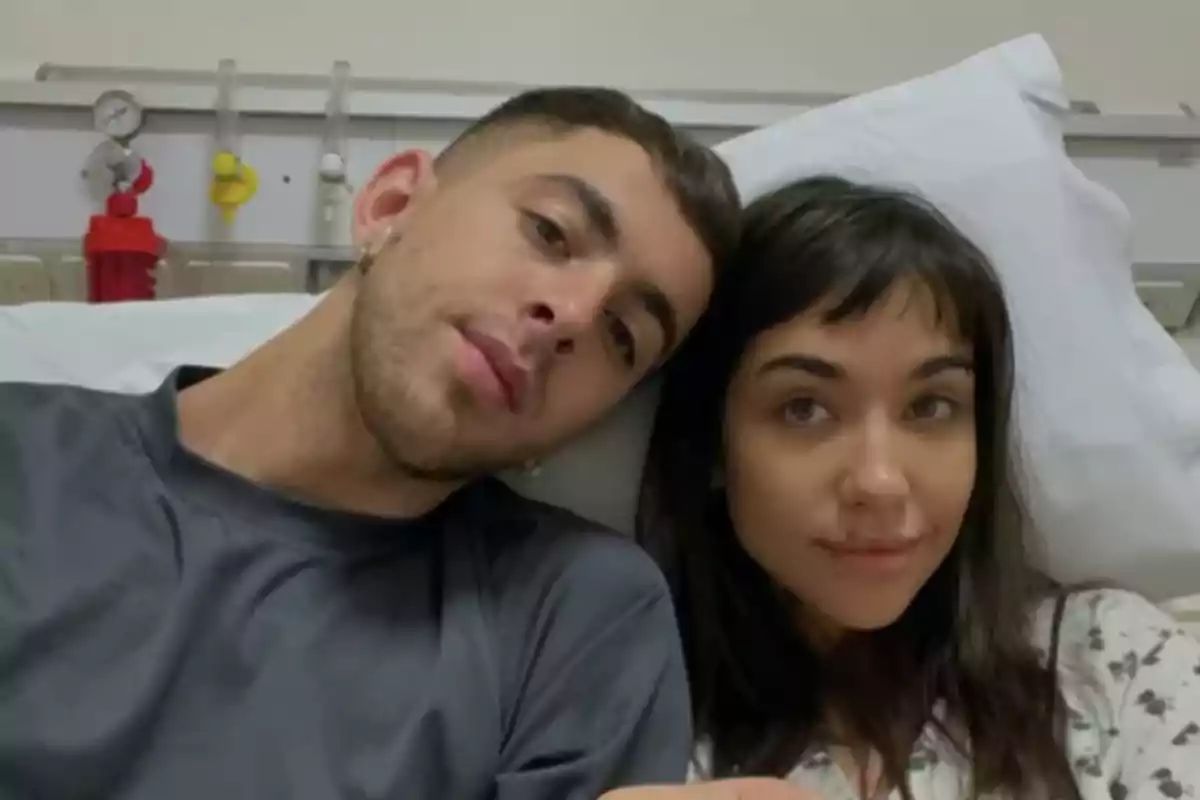 Una pareja joven está recostada en una cama de hospital, ambos miran a la cámara con expresiones serenas. Una pareja joven está recostada en una cama de hospital, ambos miran a la cámara con expresiones serenas.