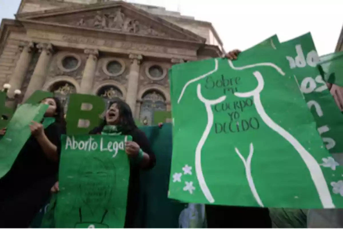 People holding green signs with messages in favor of legal abortion in front of a historic building.
