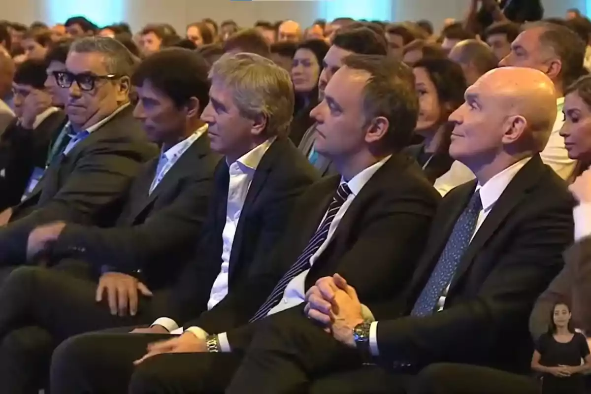 A group of people sitting at a conference, all dressed formally and paying attention to the event. A group of people sitting at a conference, all dressed formally and paying attention to the event.