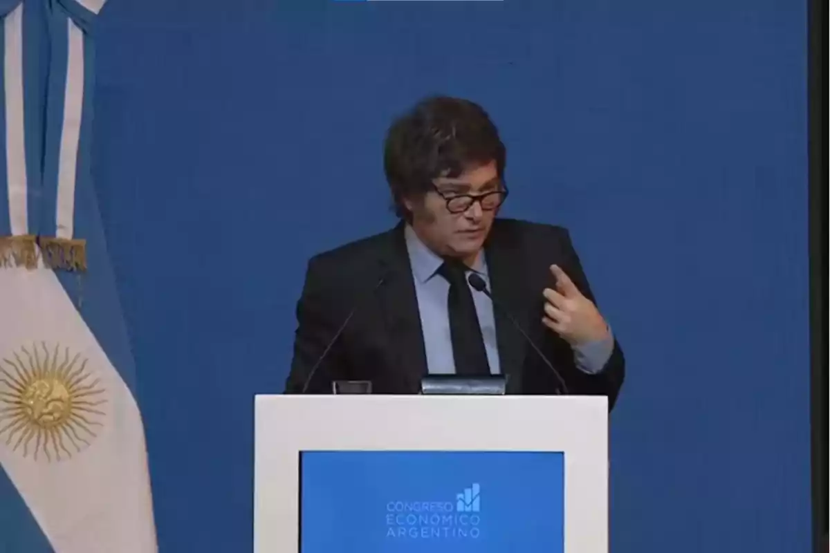 A man in a suit and tie speaks at a podium with the text A man in a suit and tie speaks at a podium with the text