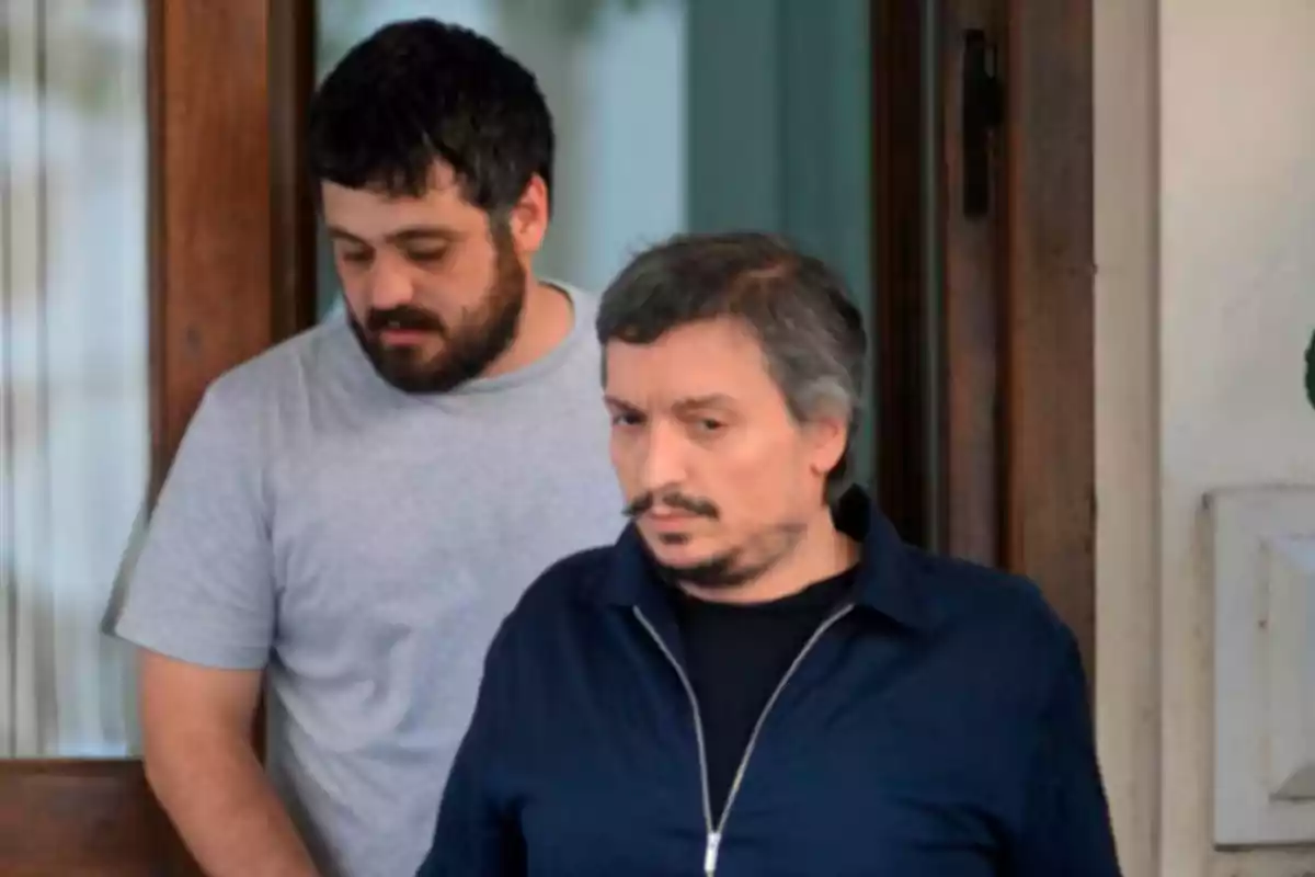 Dos hombres de pie en la entrada de un edificio, uno con camiseta gris y el otro con chaqueta azul. Dos hombres de pie en la entrada de un edificio, uno con camiseta gris y el otro con chaqueta azul.