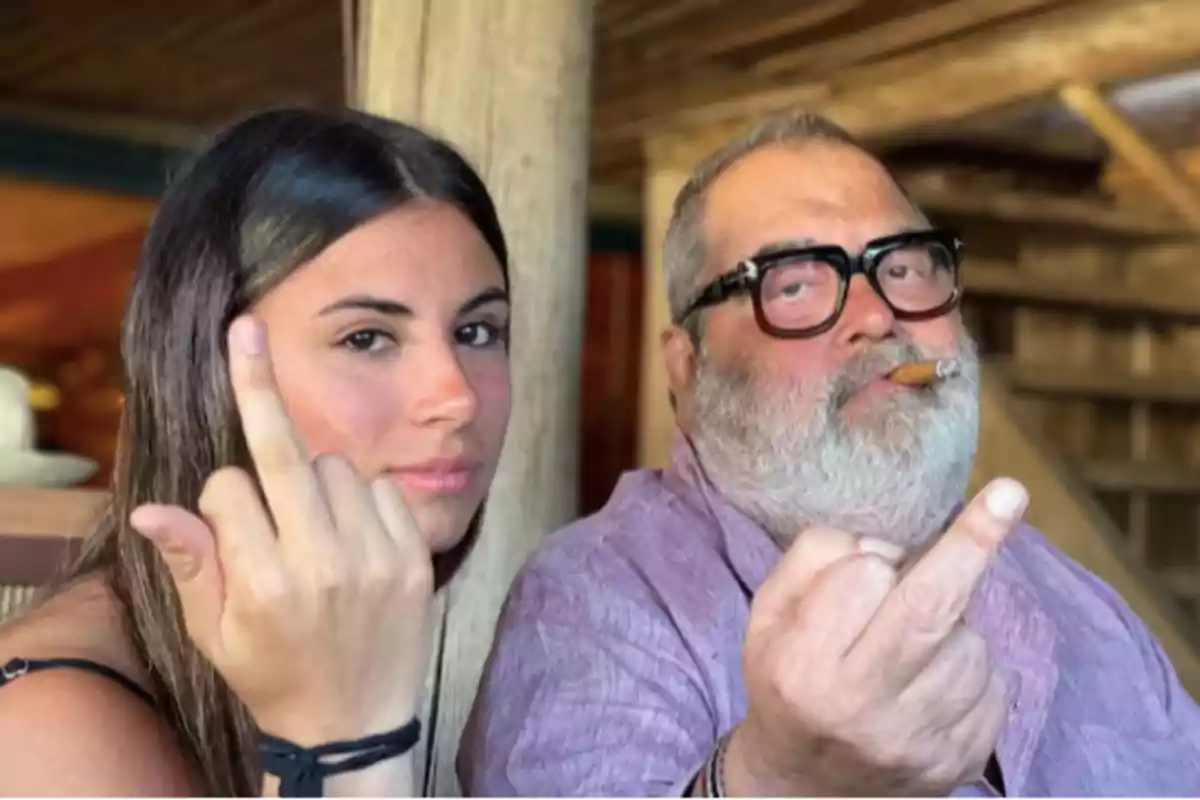 Dos personas mostrando un gesto con el dedo medio en un ambiente interior, una de ellas sostiene un cigarro.