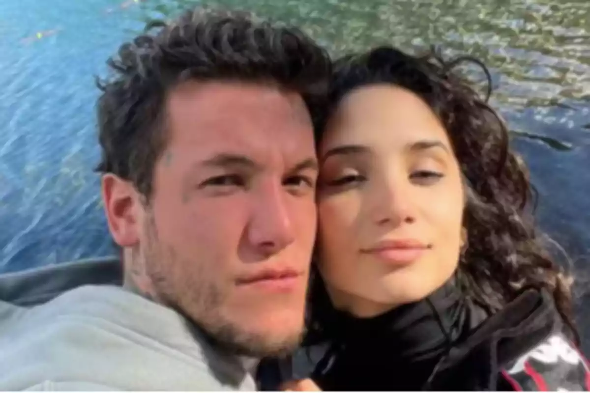 A smiling couple posing in front of a body of water.