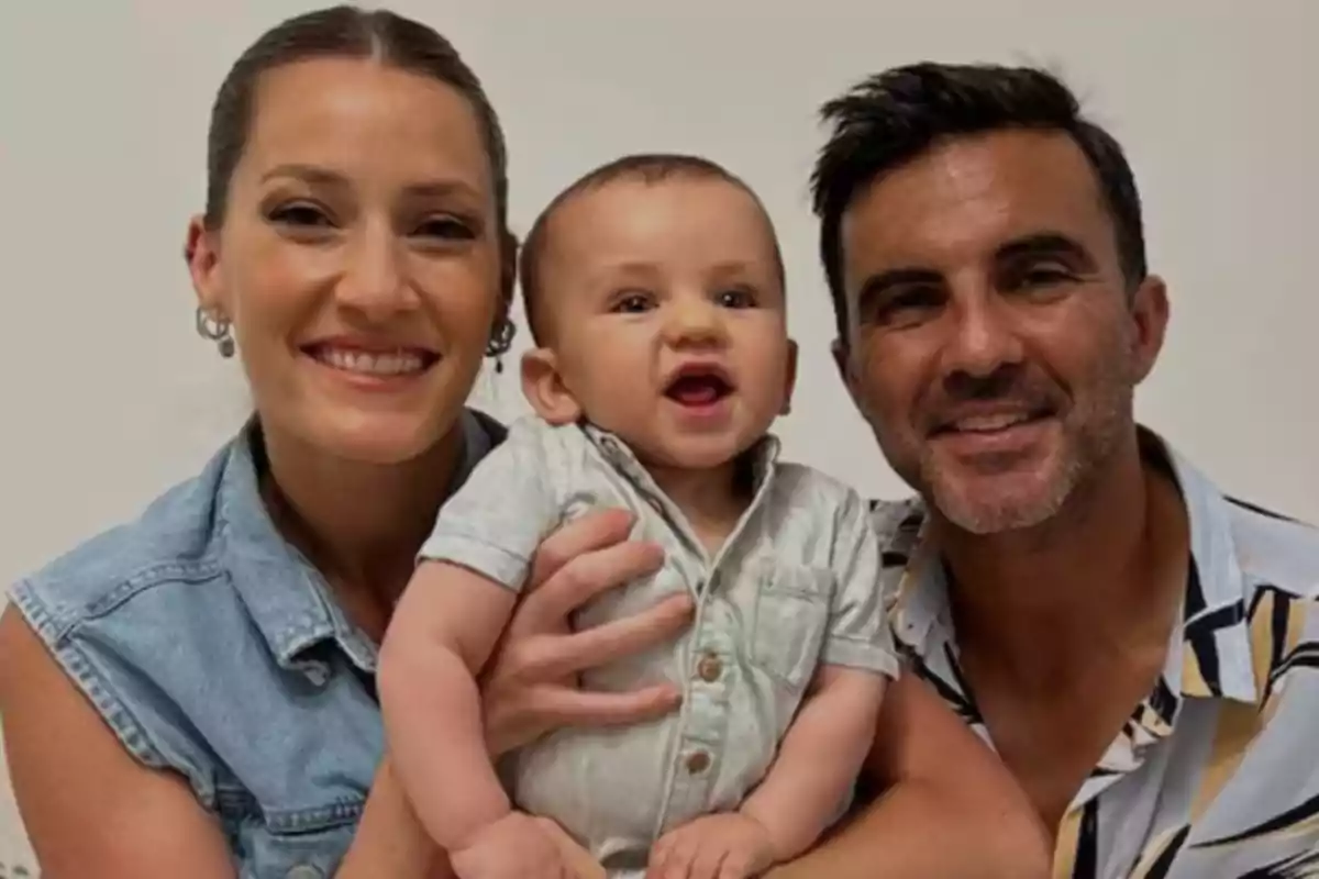A smiling family poses for the camera, with a baby in the center.
