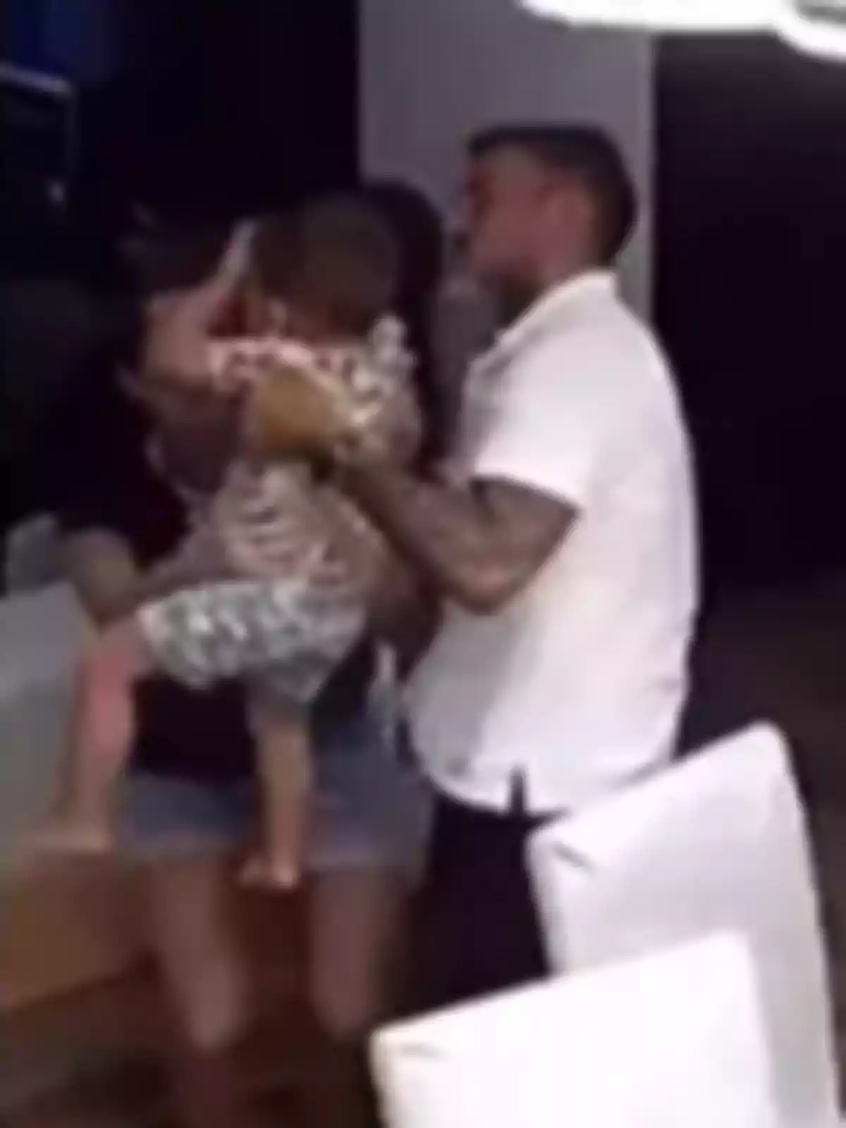 A man and a woman hold a small child in an indoor setting with white chairs. A man and a woman hold a small child in an indoor setting with white chairs.
