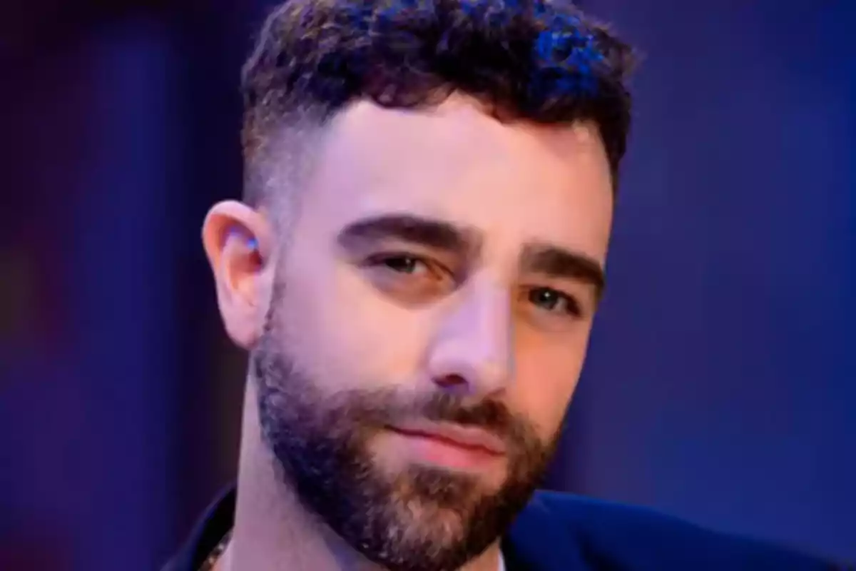 A man with a beard and curly hair looks at the camera with a neutral expression. A man with a beard and curly hair looks at the camera with a neutral expression.