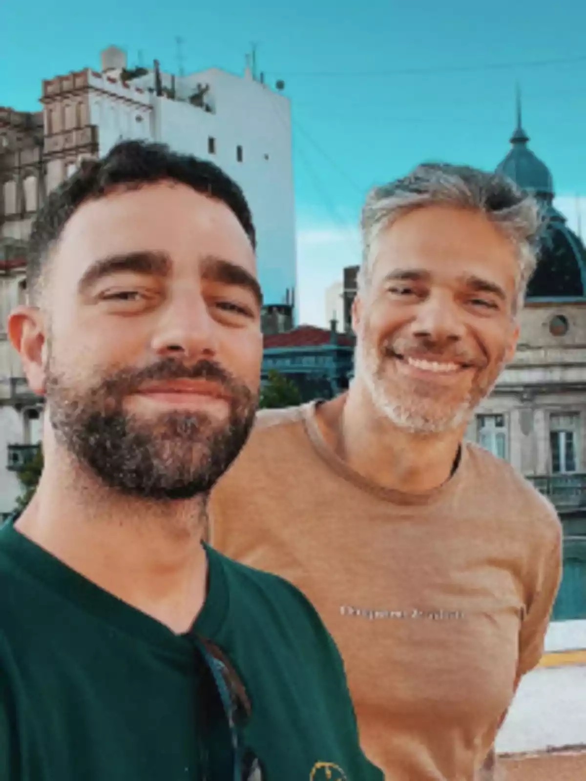 Two smiling people pose for a selfie outdoors with buildings in the background. Two smiling people pose for a selfie outdoors with buildings in the background.