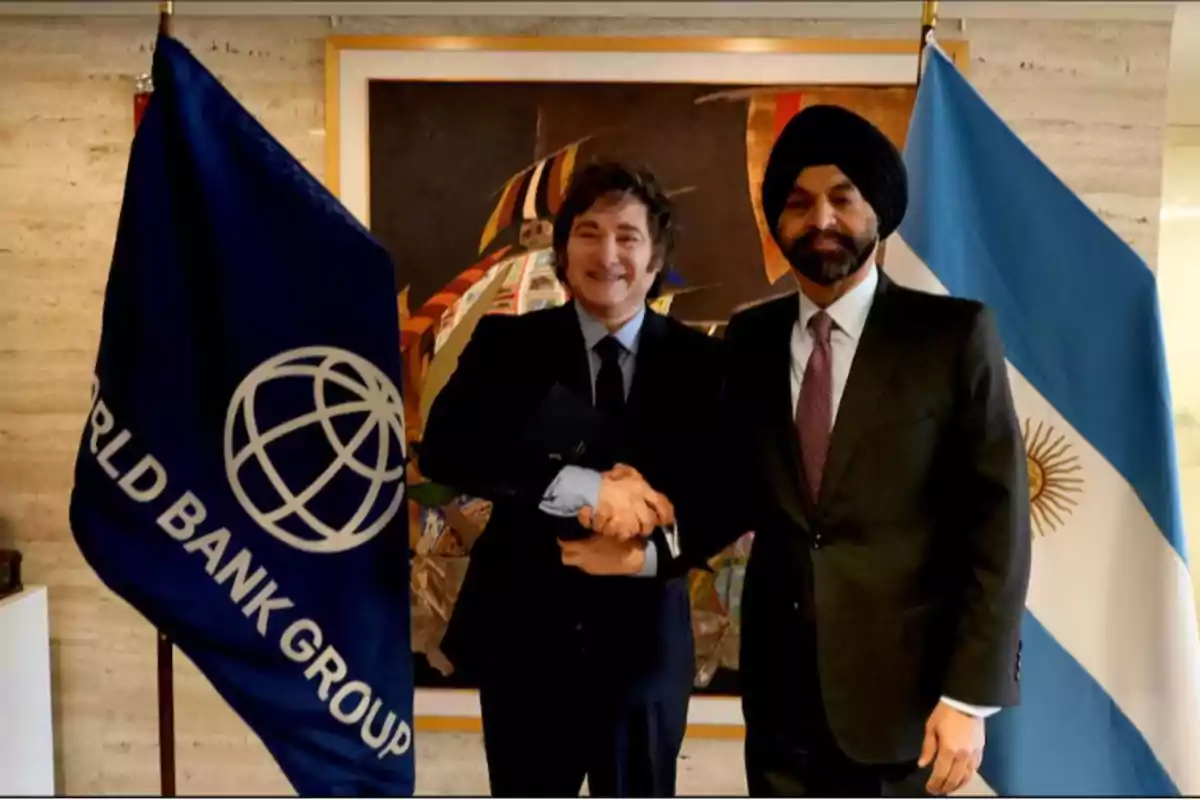 Two men in suits shake hands in front of the World Bank and Argentina flags.