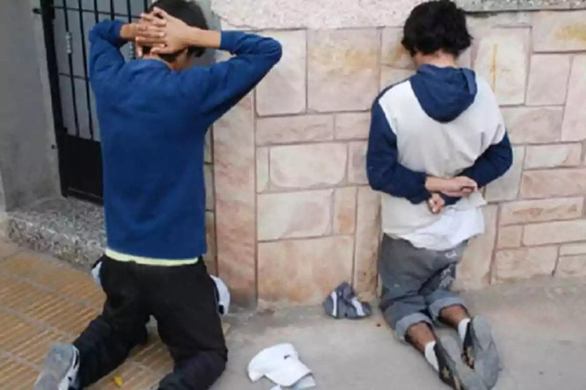 Dos personas arrodilladas contra una pared con las manos detrás de la cabeza. Dos personas arrodilladas contra una pared con las manos detrás de la cabeza.