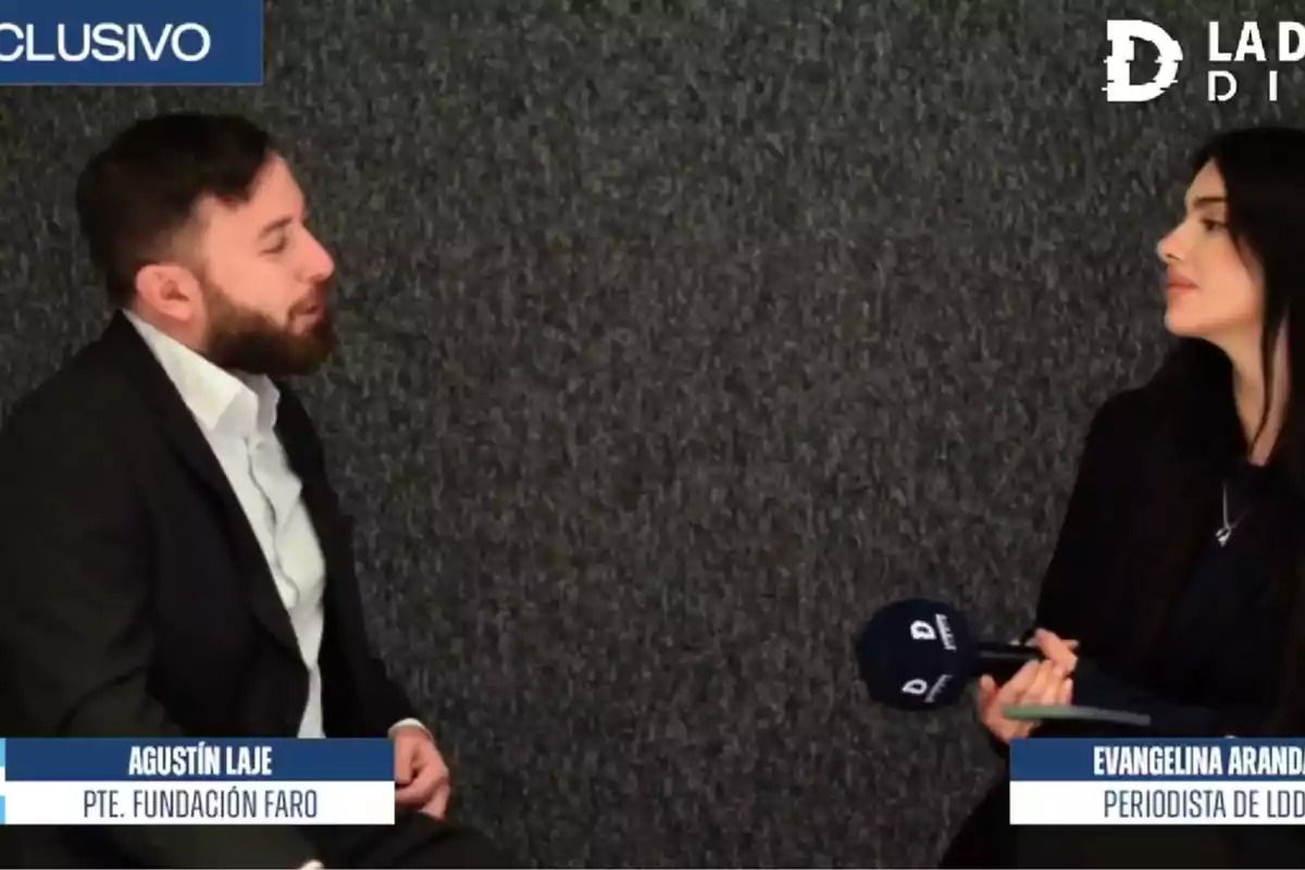 Dos personas sentadas frente a frente en una entrevista, una de ellas sostiene un micrófono. Dos personas sentadas frente a frente en una entrevista, una de ellas sostiene un micrófono.