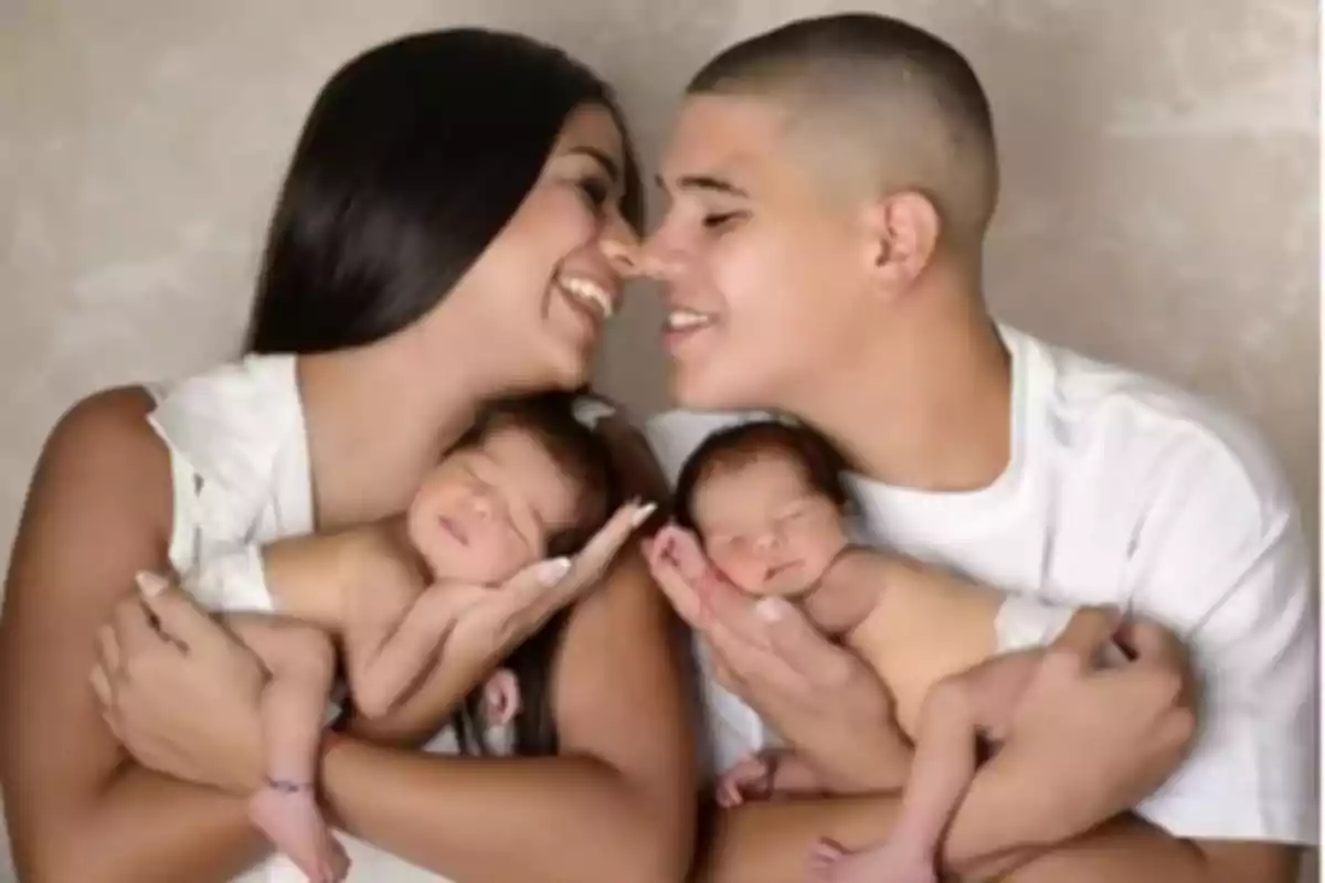 Una pareja sonriente sostiene a dos bebés recién nacidos en sus brazos. Una pareja sonriente sostiene a dos bebés recién nacidos en sus brazos.
