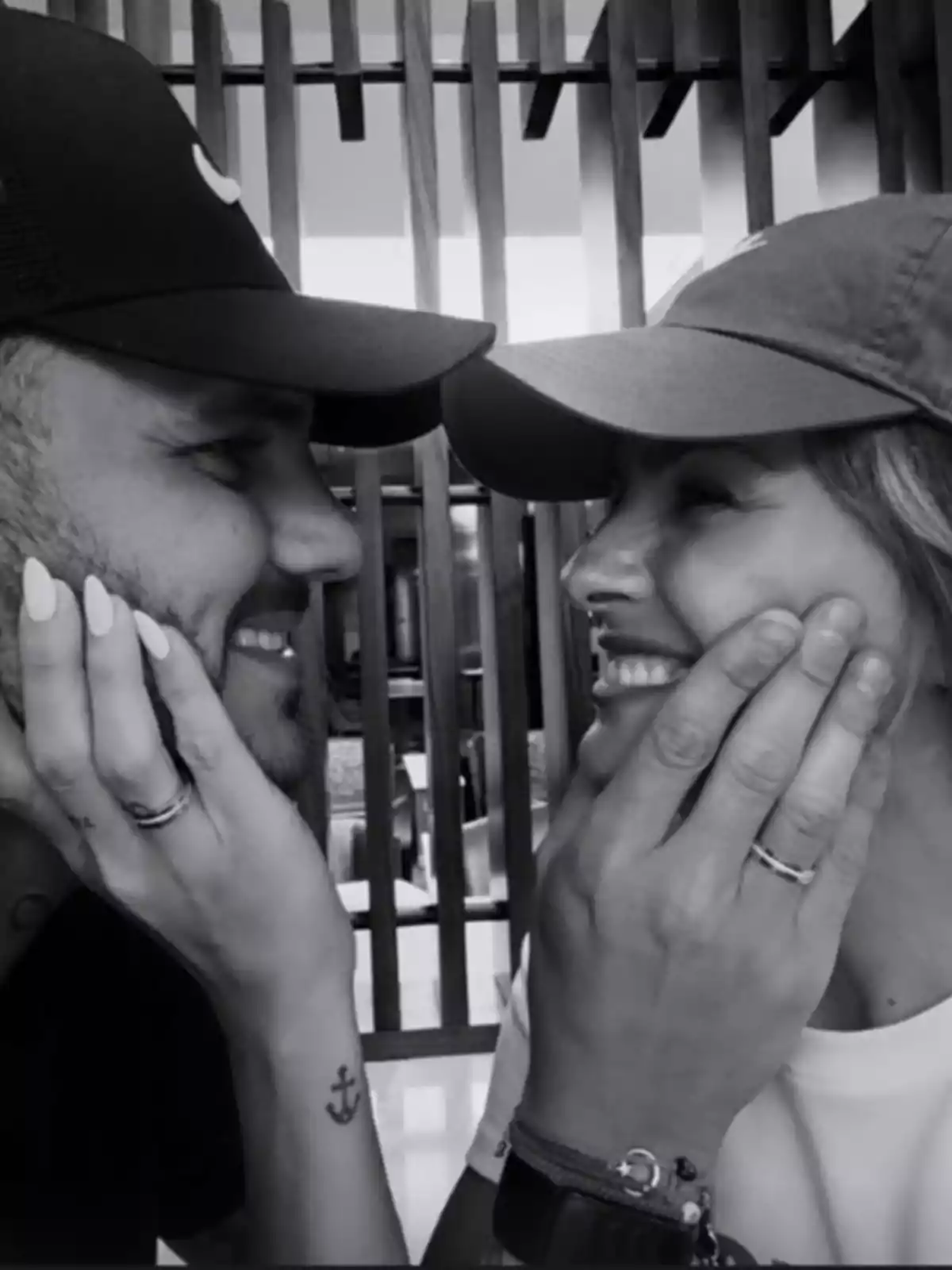 Two people with caps smile at each other while holding each other's faces. Two people with caps smile at each other while holding each other's faces.