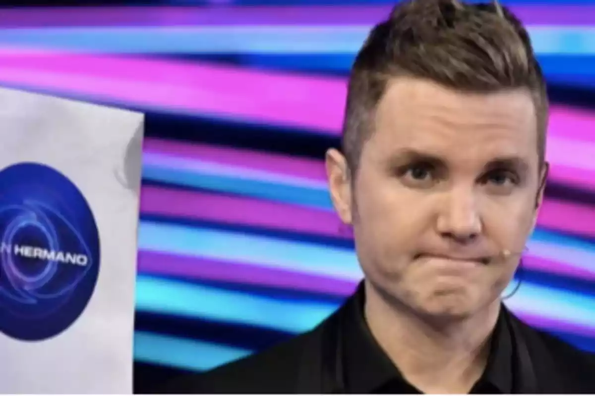 Un presentador de televisión con expresión seria sostiene un sobre con el logo de un programa en un fondo colorido. Un presentador de televisión con expresión seria sostiene un sobre con el logo de un programa en un fondo colorido.