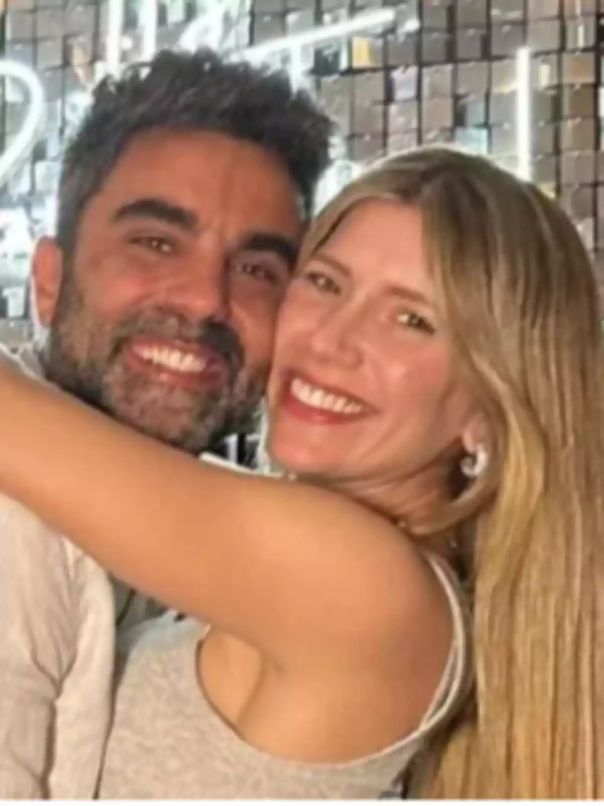 Dos personas sonrientes abrazándose frente a un fondo con luces brillantes. Dos personas sonrientes abrazándose frente a un fondo con luces brillantes.