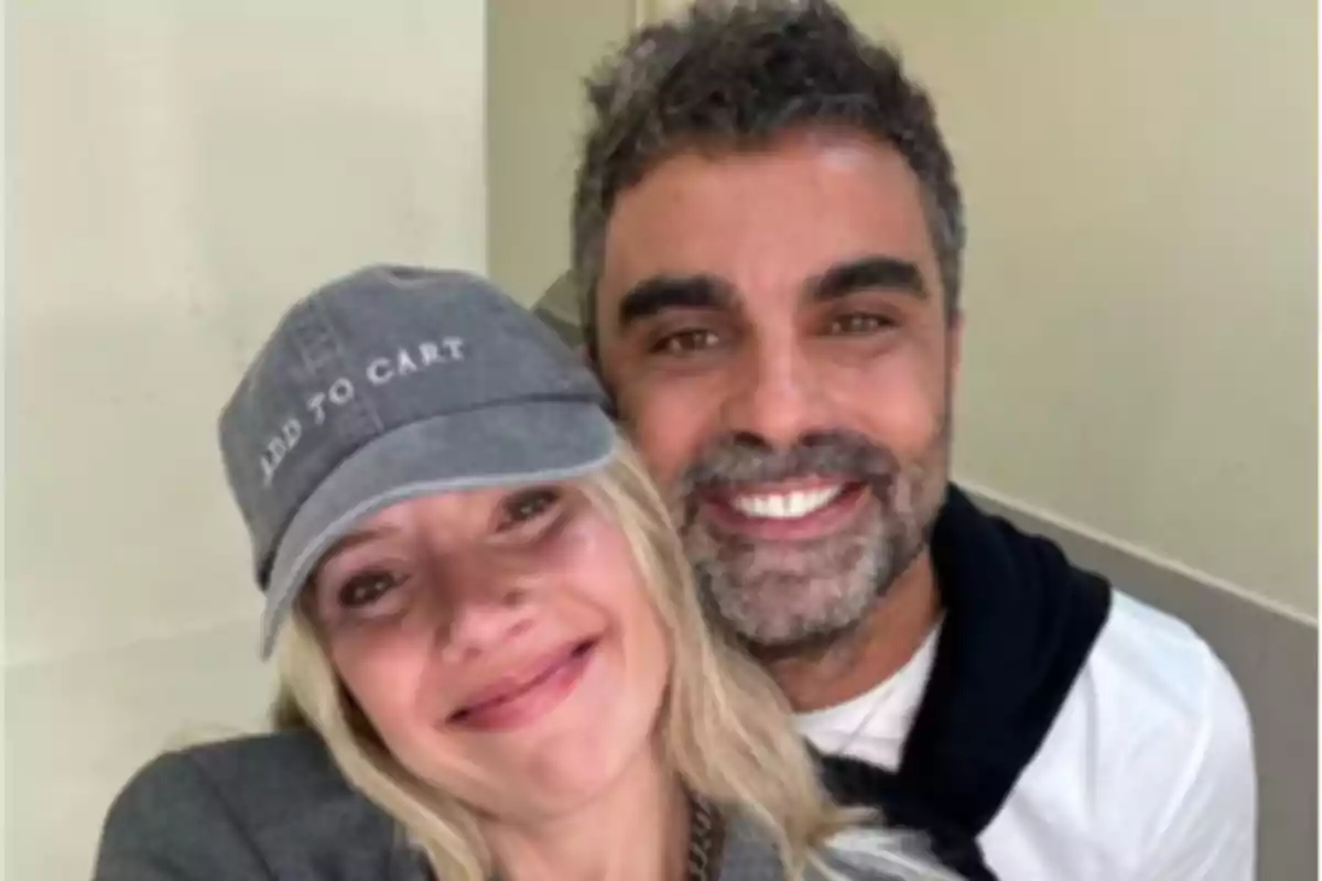Una pareja sonriente posando para una selfie, la mujer lleva una gorra gris con la frase Una pareja sonriente posando para una selfie, la mujer lleva una gorra gris con la frase