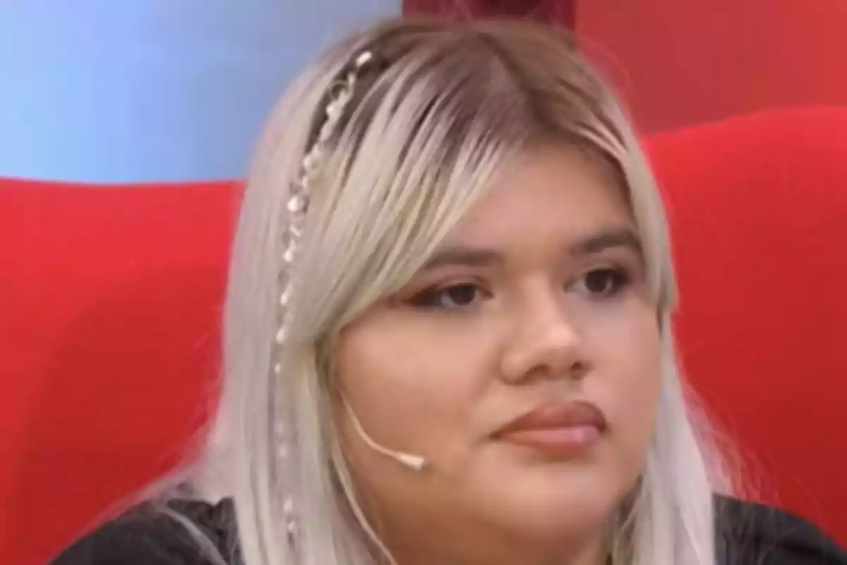 Una persona con cabello rubio y un micrófono en la oreja está sentada en un sillón rojo. Una persona con cabello rubio y un micrófono en la oreja está sentada en un sillón rojo.